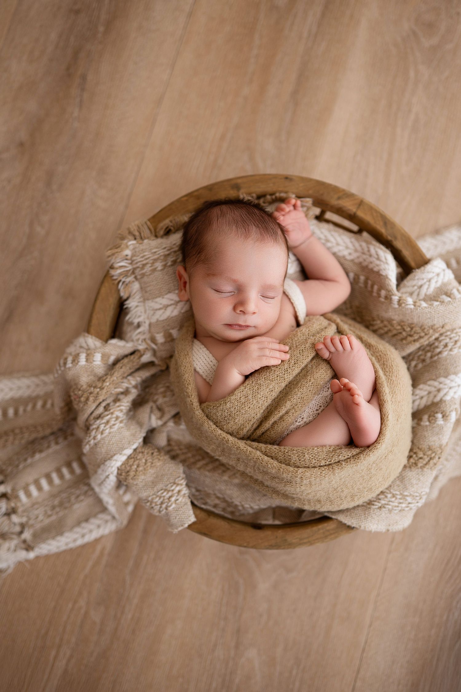 Newborn photography series showing sleeping baby wrapped in beige fabric on wooden bowl against neutral background.