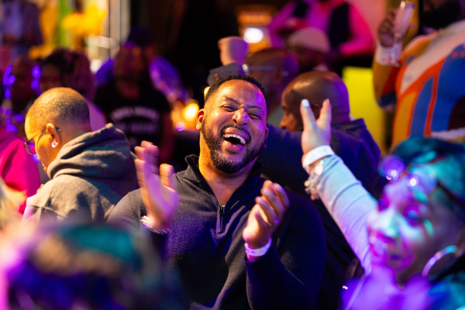 People dancing and clapping at a vibrant nightclub with colorful lighting and energetic atmosphere.