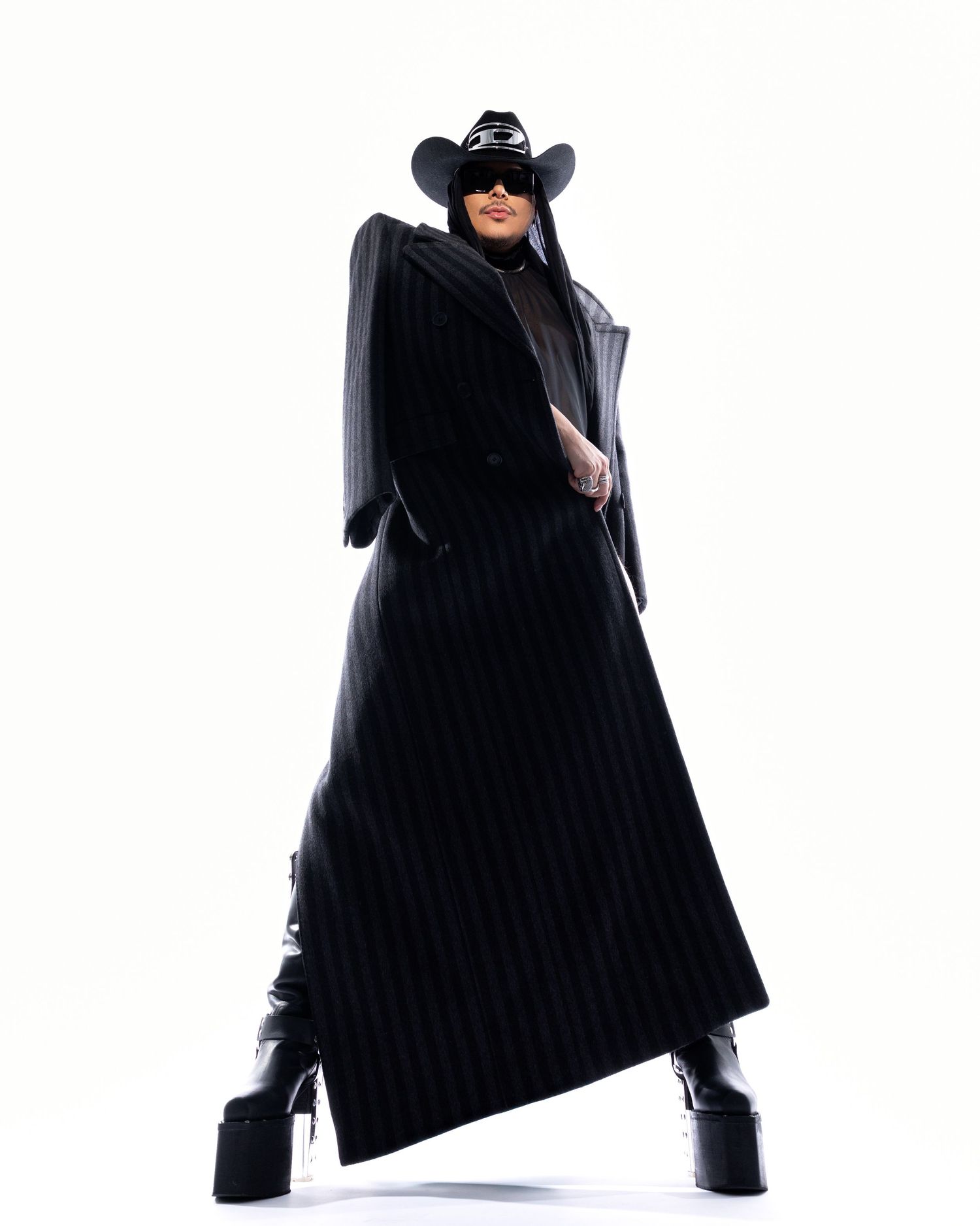 Person wearing black cape and cowboy boots striking dynamic poses against white background for fashion photoshoot.