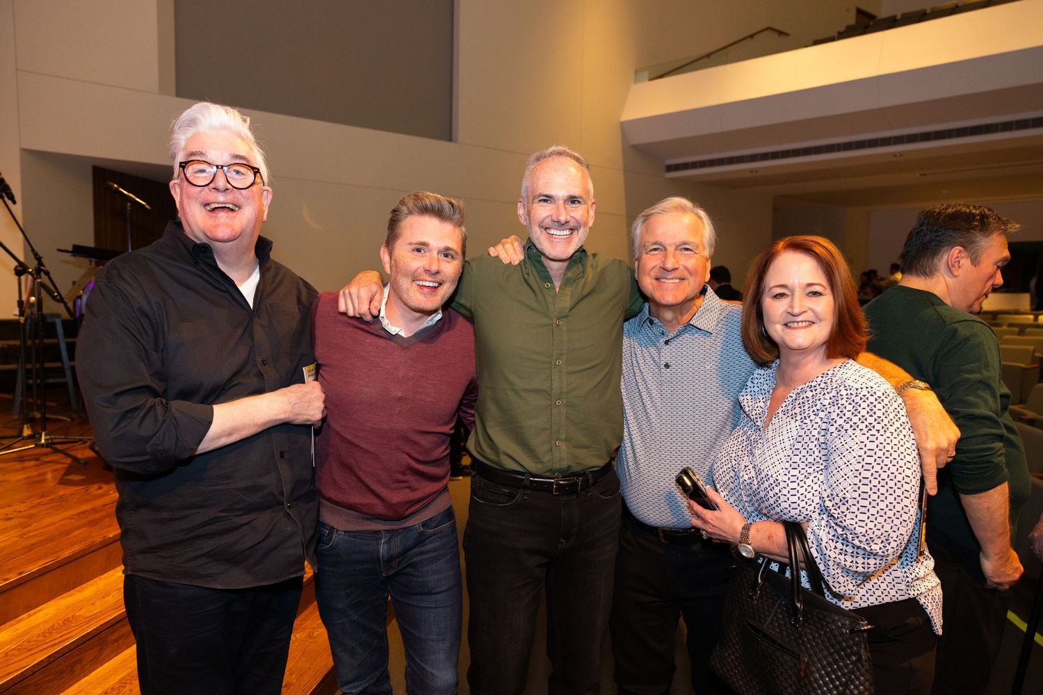 A group stands together smiling at a social gathering in a wood-paneled room.
