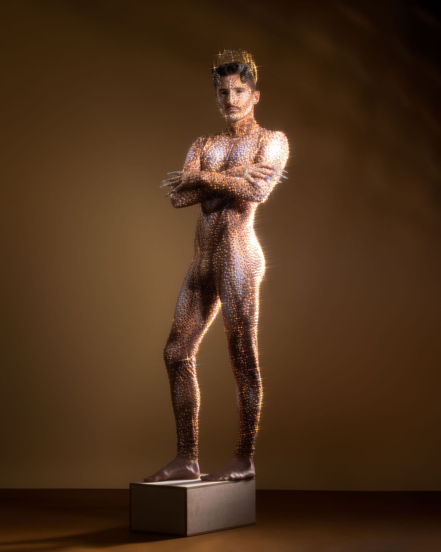 A gilded human statue covered in metallic body paint stands posed with arms crossed on a pedestal.
