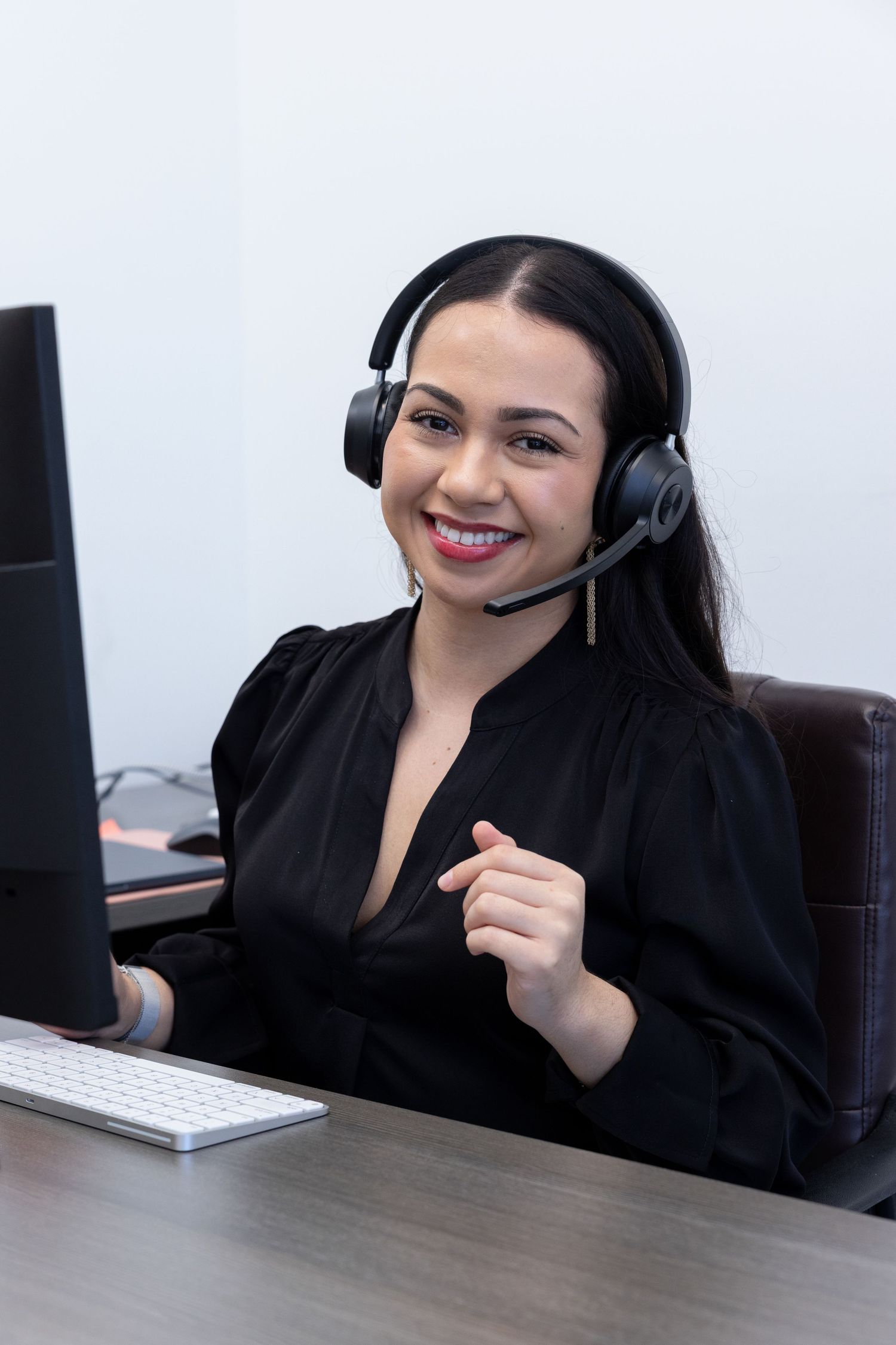 Smiling female call center agent wearing headset at desk with computer, providing customer support.