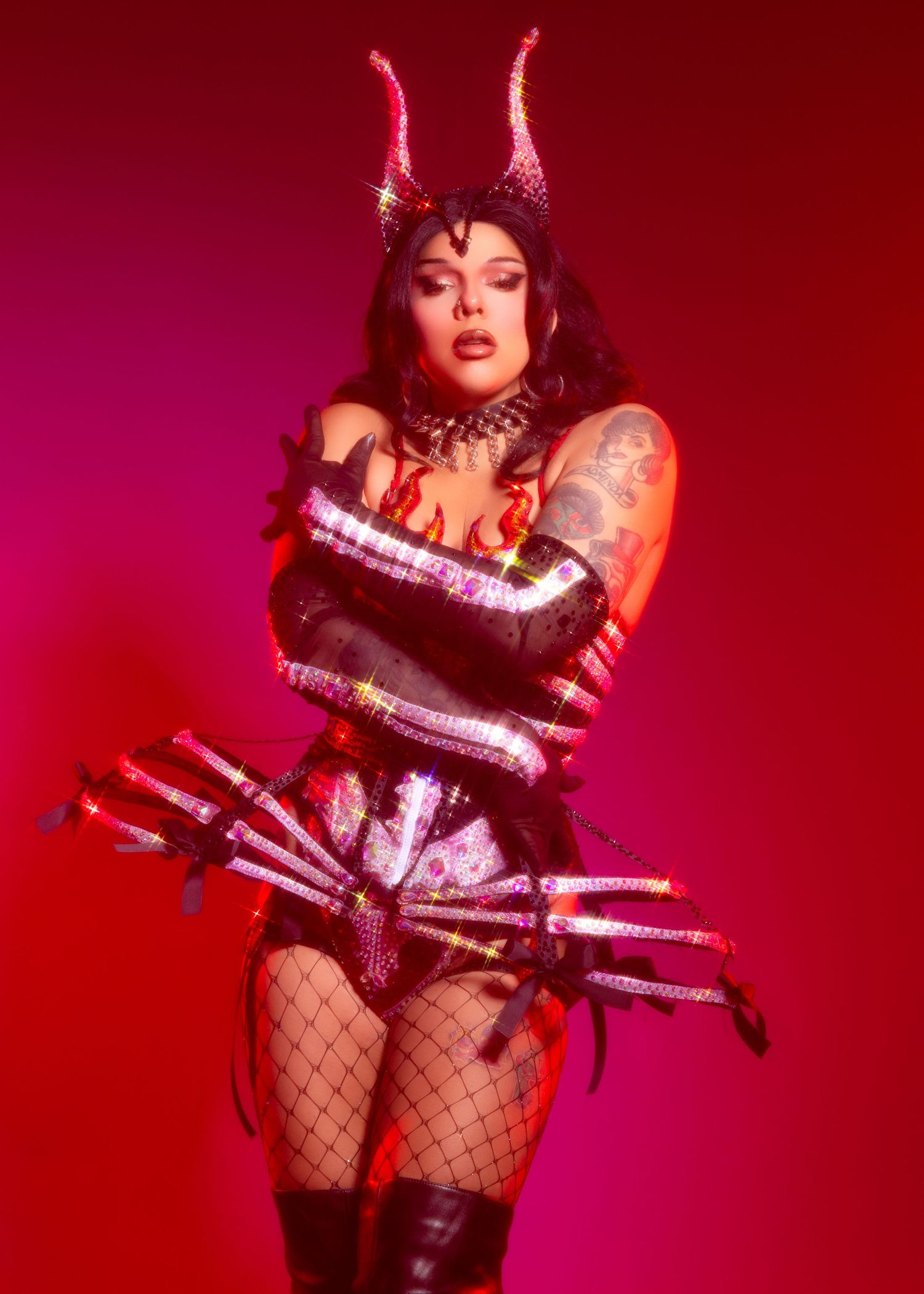 Dark gothic costume with horned headpiece, fishnet stockings and metallic details against a deep red background.