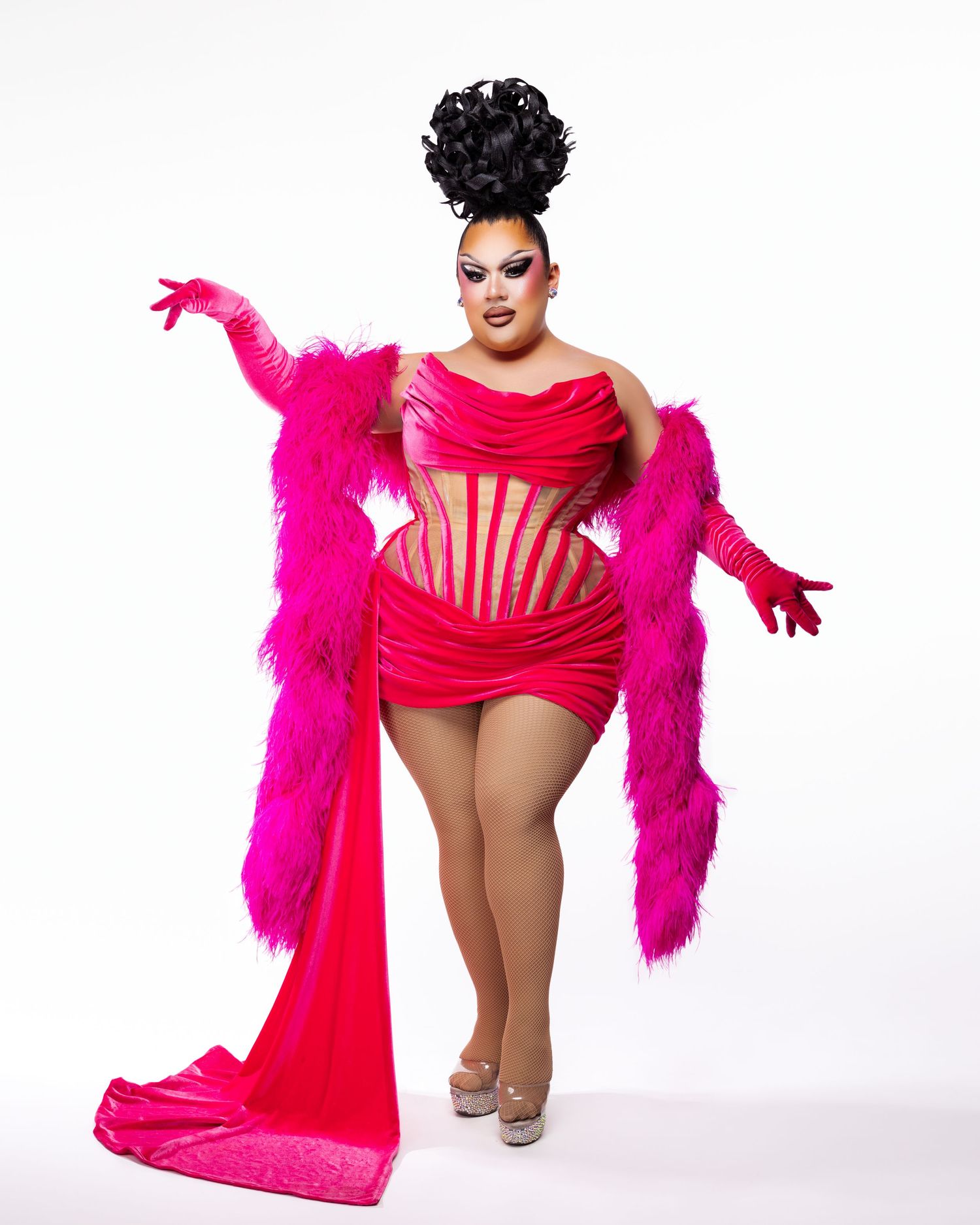 Drag performer in hot pink corset mini dress with feather boa, dramatic black updo, and pink gloves posing confidently.