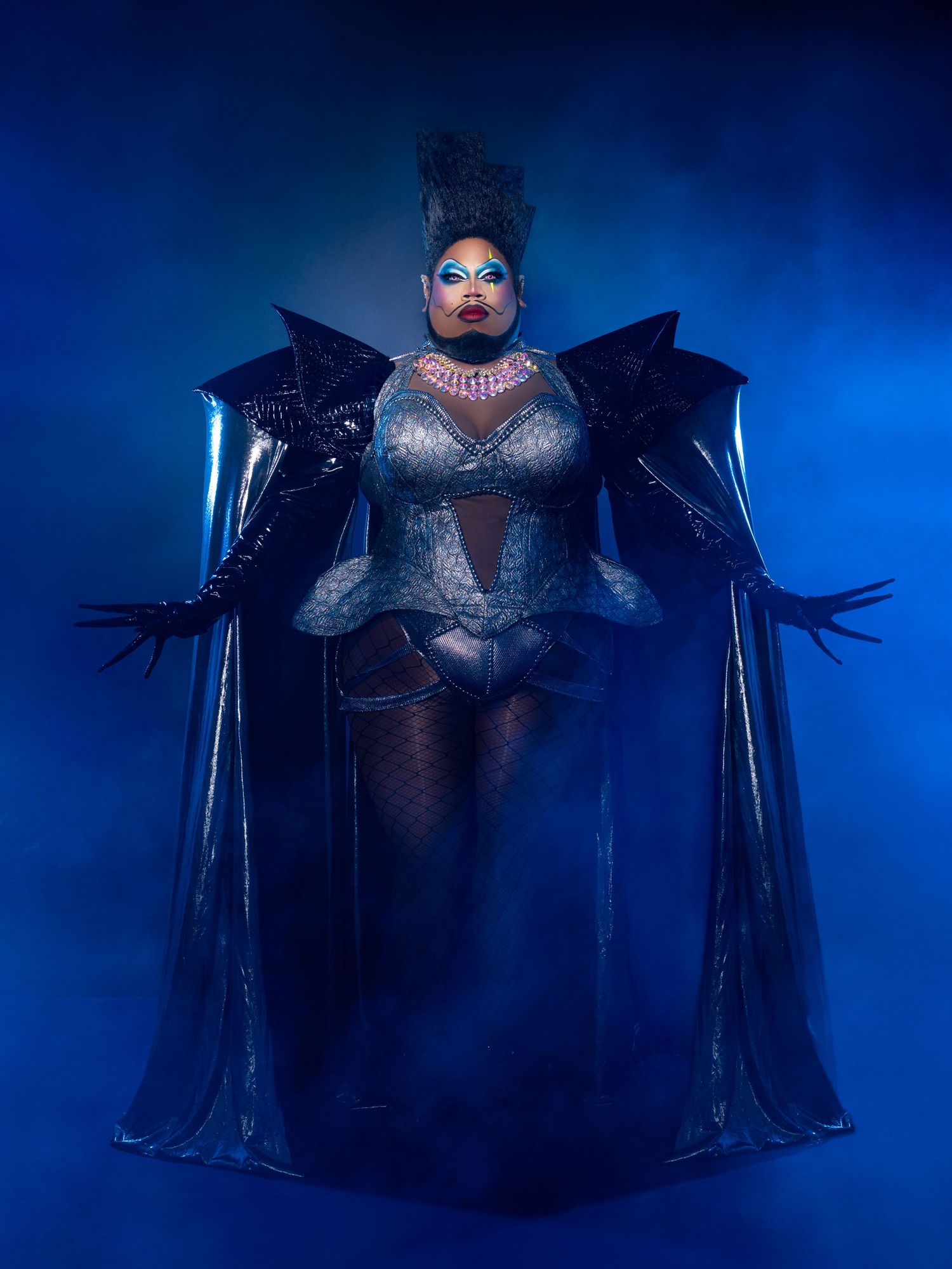 Dramatic fashion portrait in deep blue lighting featuring a gothic-inspired black winged costume with dramatic silhouette.