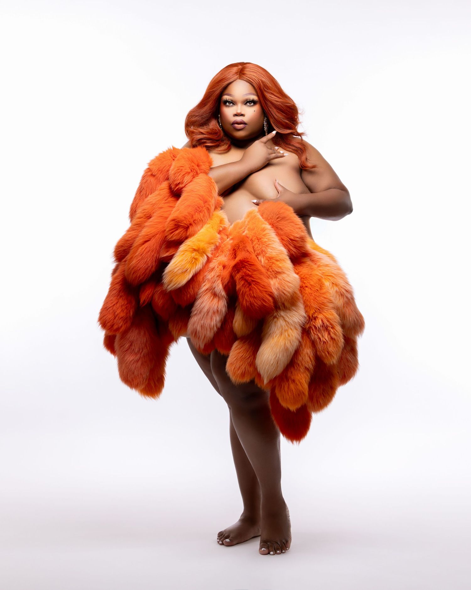 A figure draped in vibrant orange fur garments poses artistically against a white background.