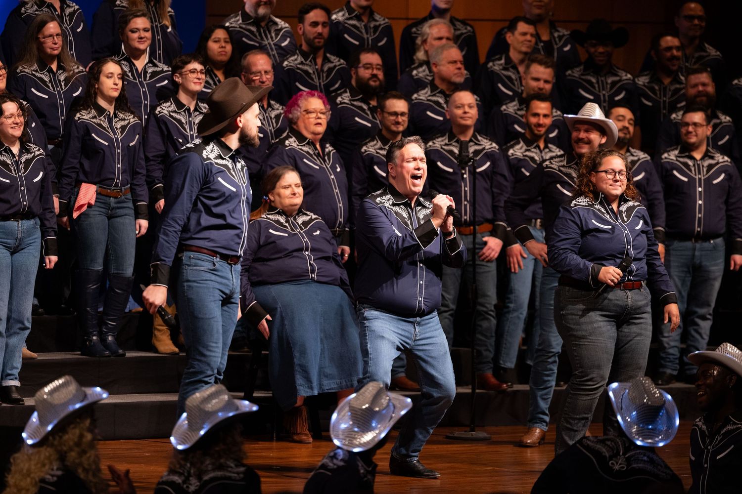 A large group of students in navy blue jackets perform together in an auditorium during a musical event.