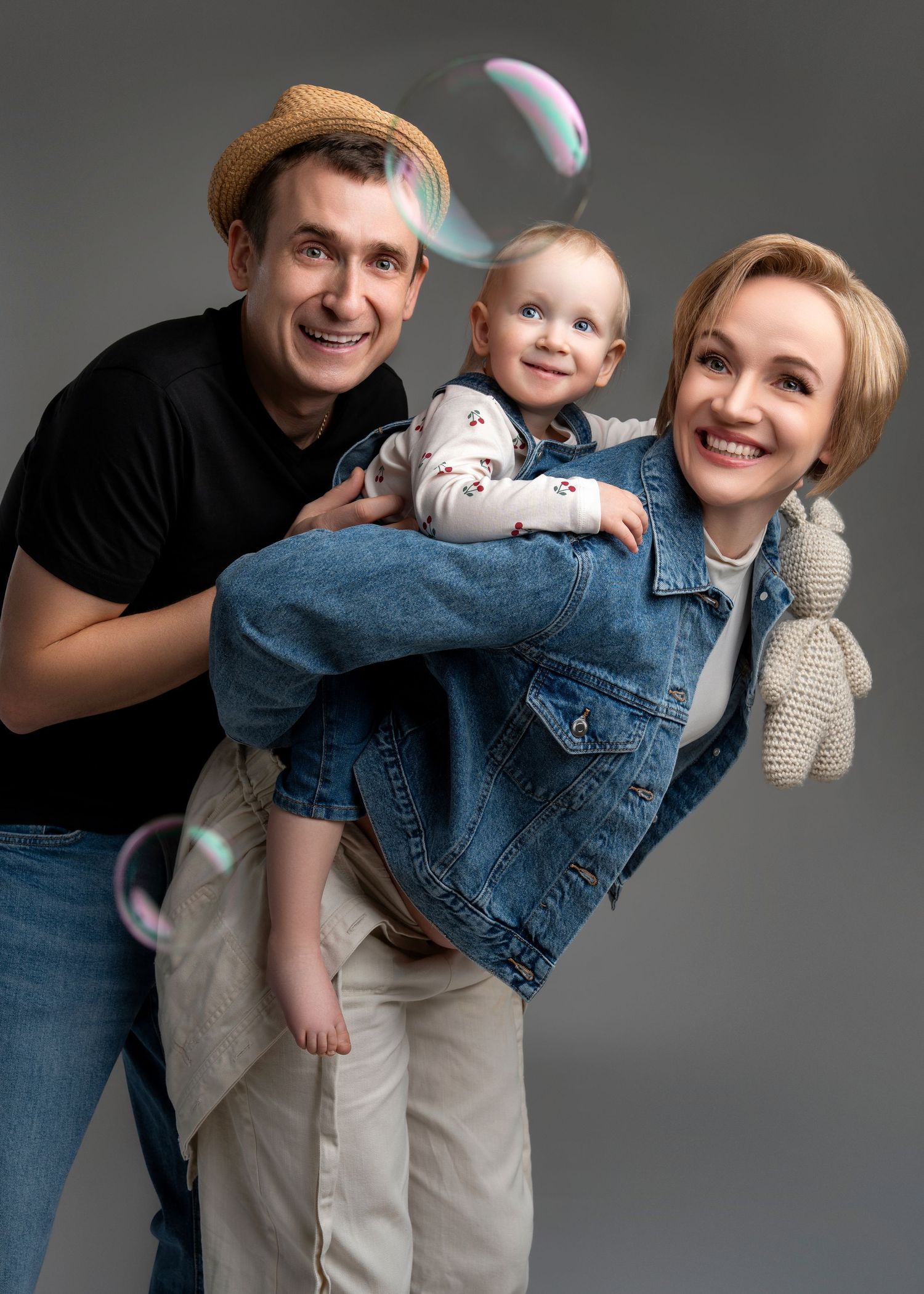 A young family embracing and smiling together during a studio photoshoot against a gray background.