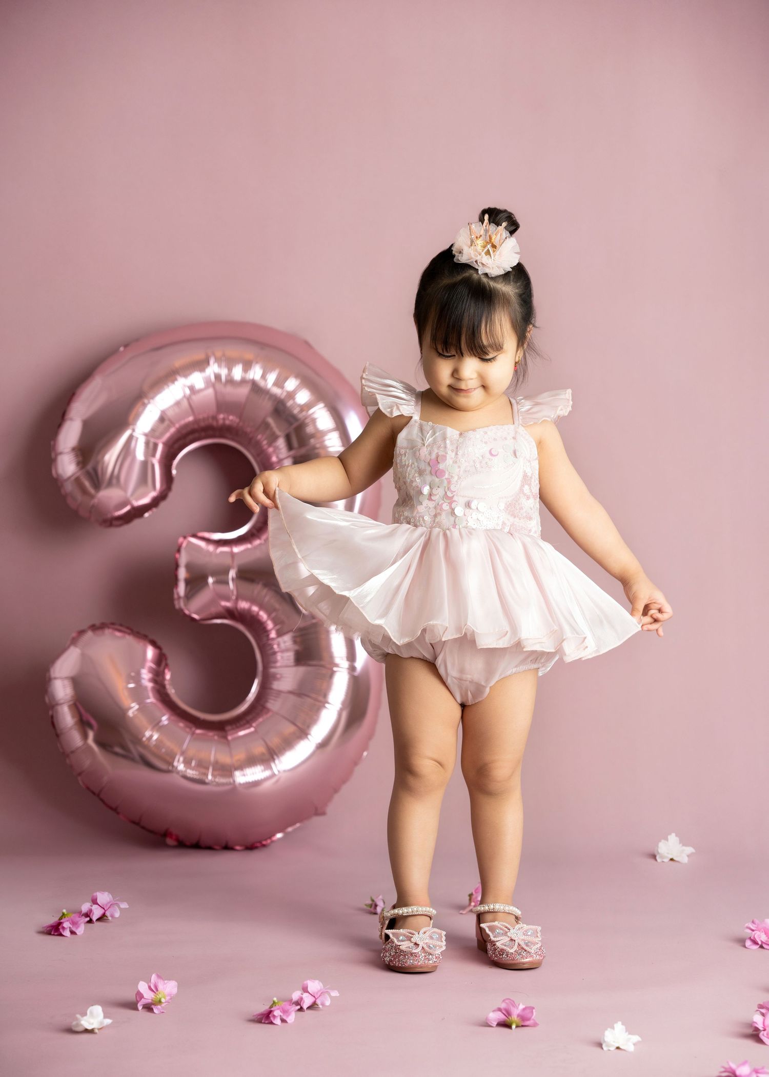 a young girl lifts the side of her skirt while standing next to a 3 shaped balloon