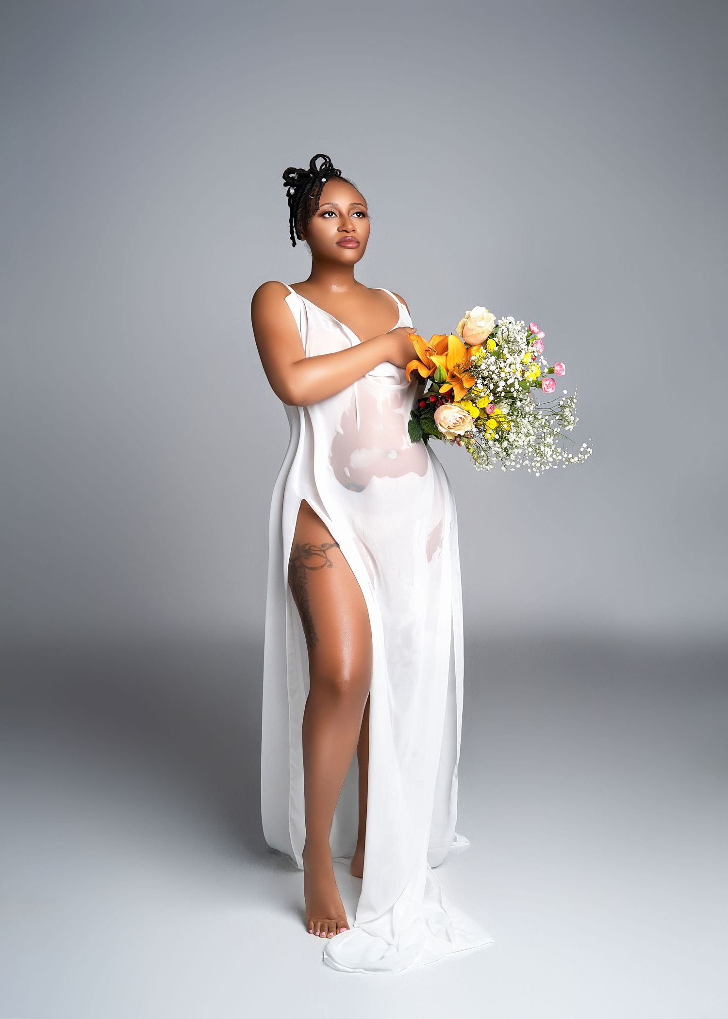 a pregnant woman stands in a wet white dress while holding flowers from a session with a minneapolis photographer