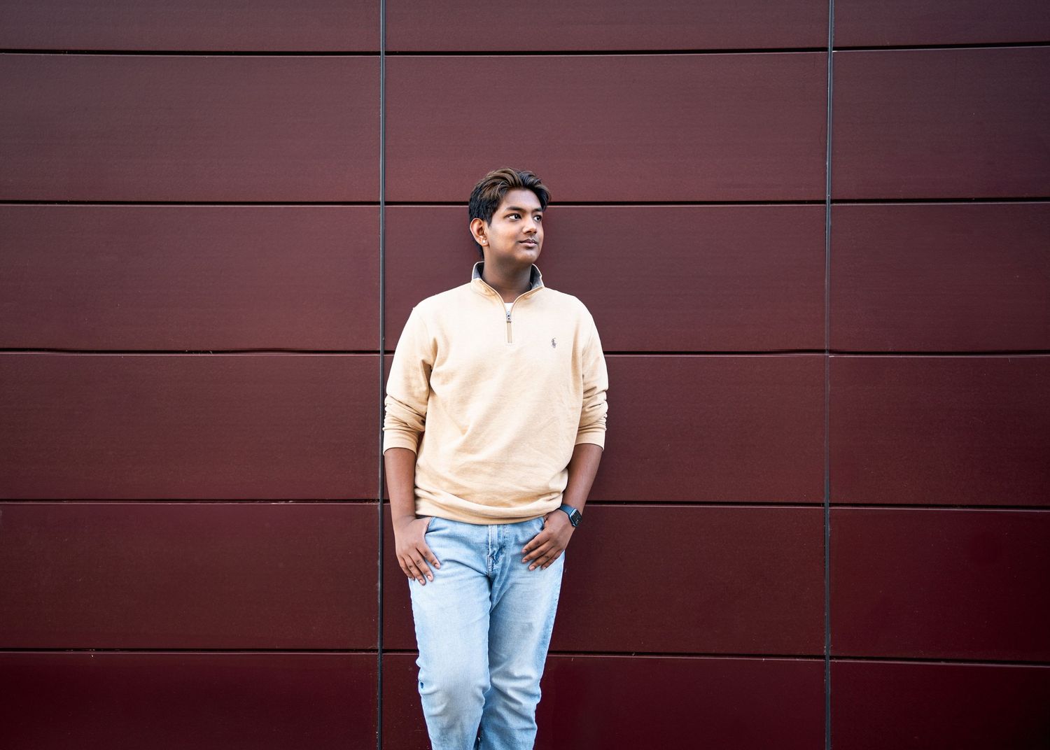 Someone wearing a yellow sweater and light jeans stands casually against a dark wall for a minneapolis senior photographer