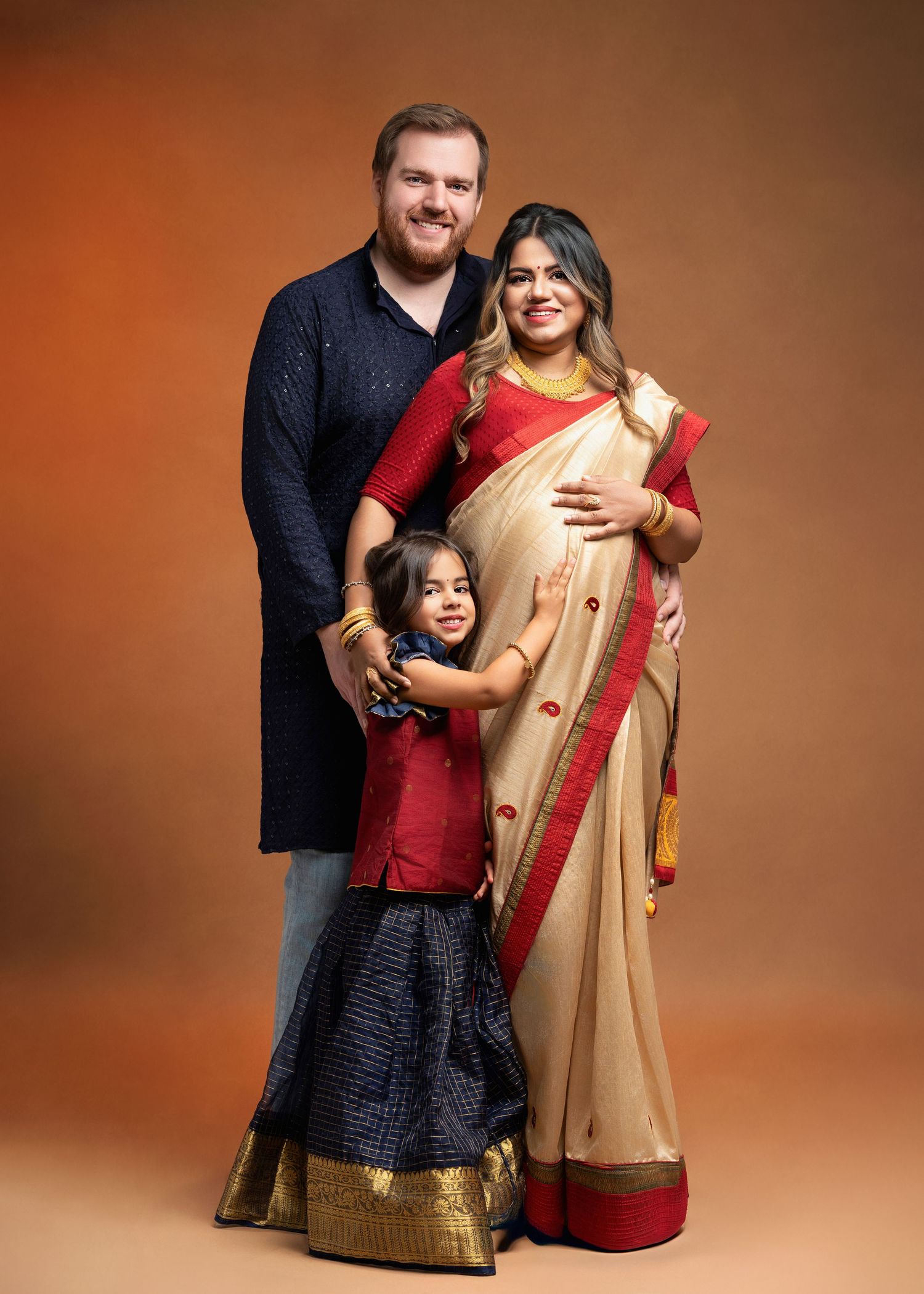 a family dressed in traditional indian garb smiles together in the studio with a minneapolis photographer