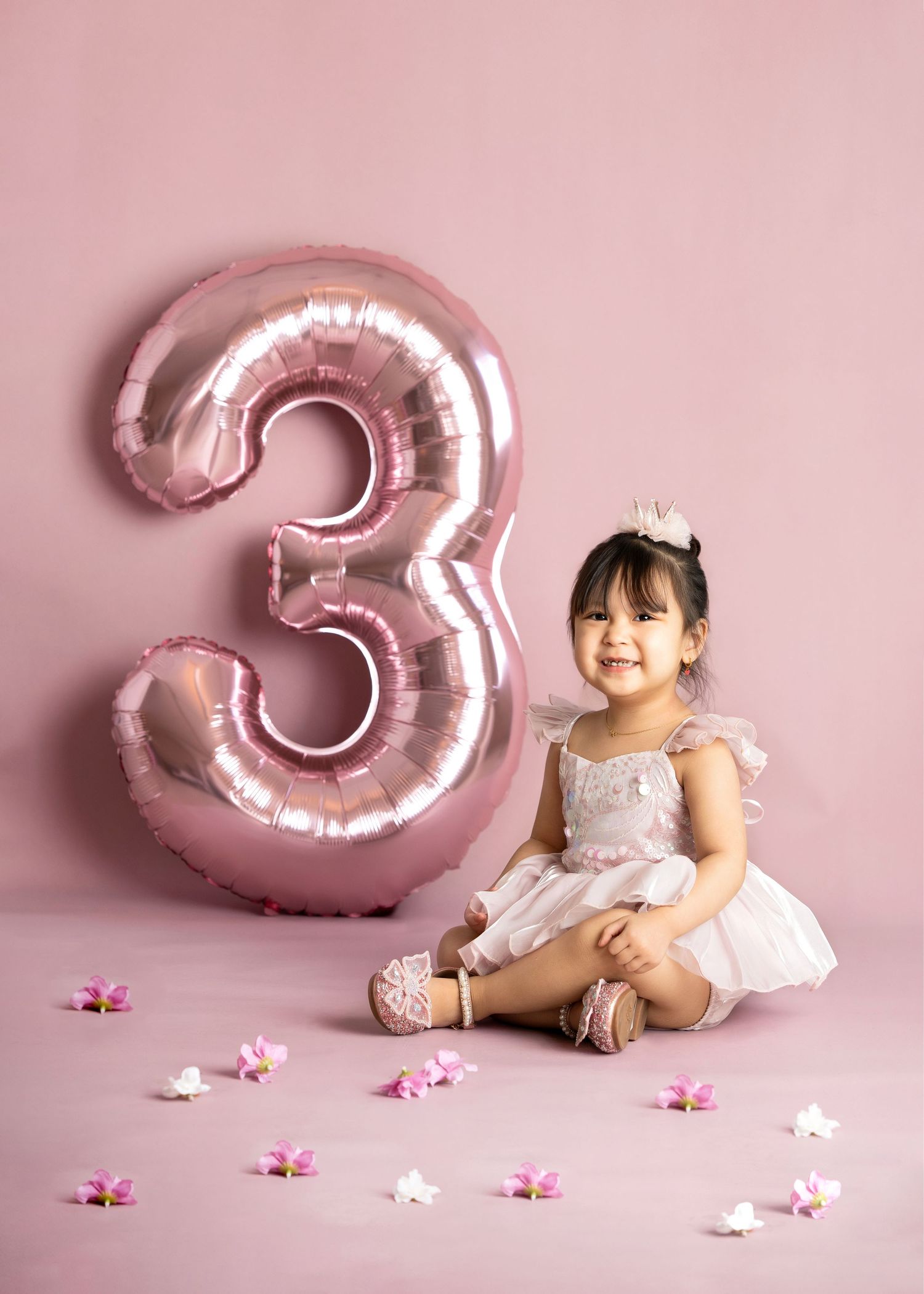 a young girl sits in a pink studio with a pink 3 shaped balloon for a minneapolis milestone photographer