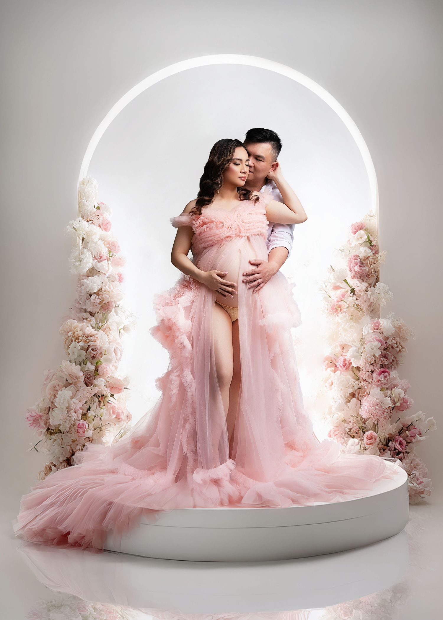 Maternity photoshoot with pink flowing gowns set against a white circular backdrop with floral decorations by Minnesota photographer