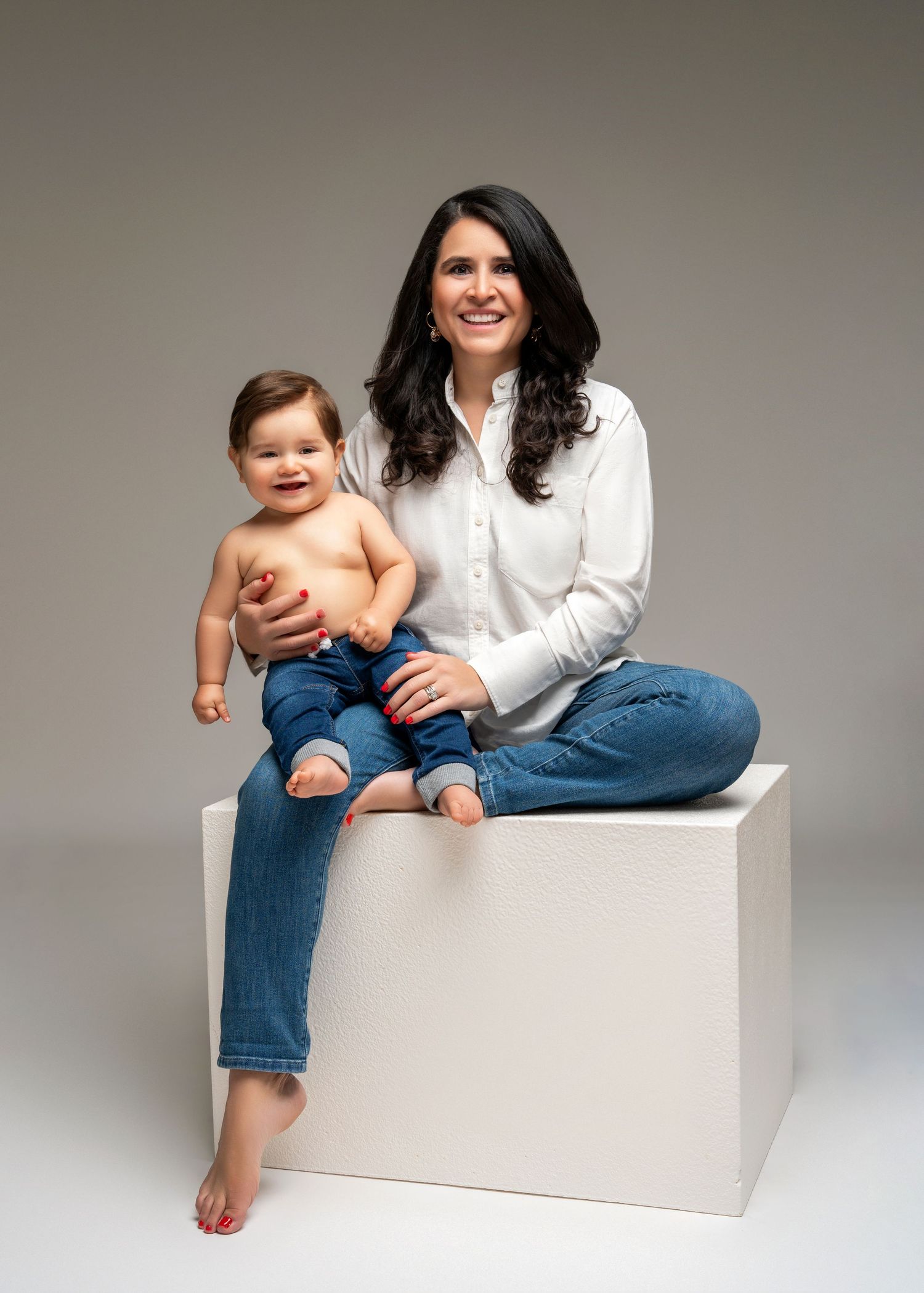 a mom sits with her son on a white cube in the studio with a motherhood photographer