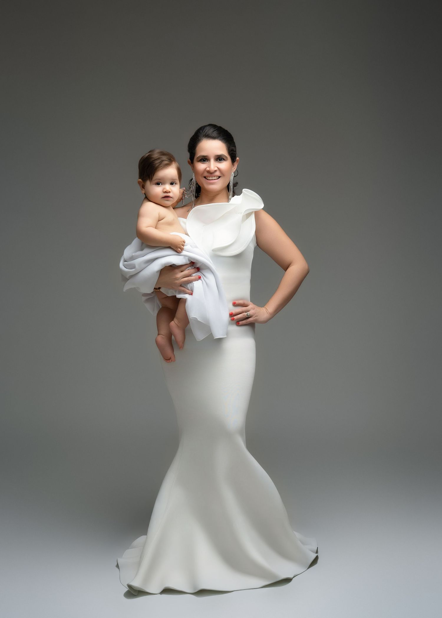 a mother stands in a white gown while holding her child for a motherhood photographer in minneapolis minnesota