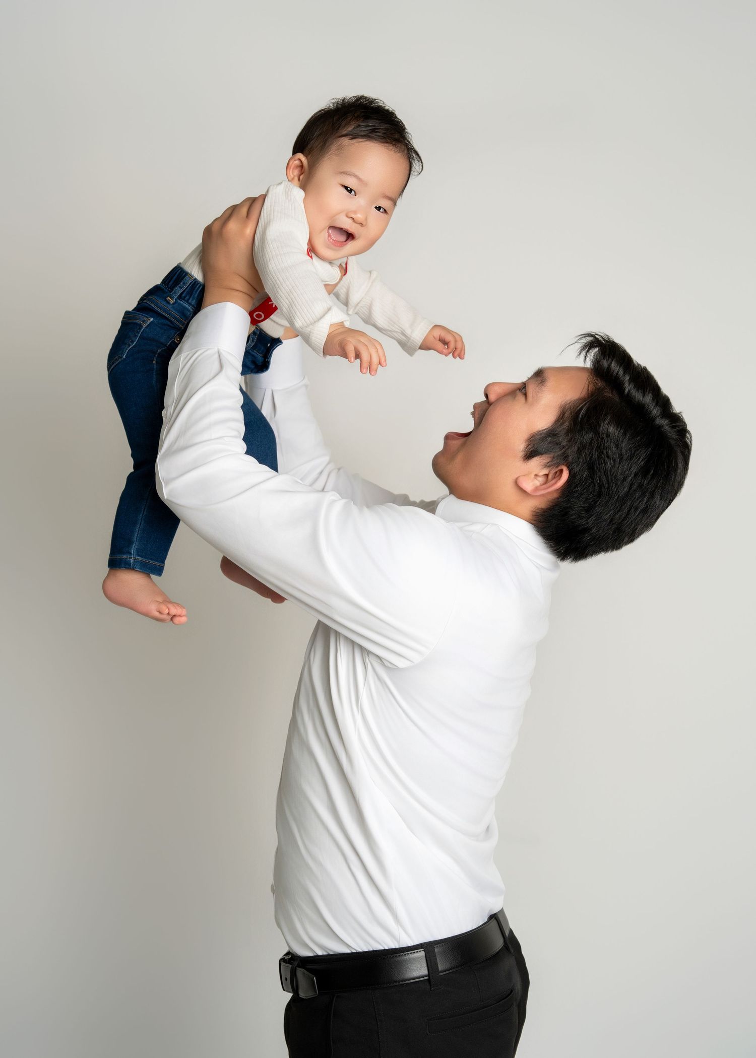 a father lifts his infant son above his head as they smile
