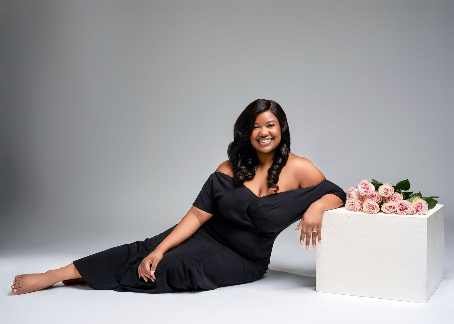 a woman lays in a white studio in a black dress for her birthday photos with a milestone photographer in minneapolis