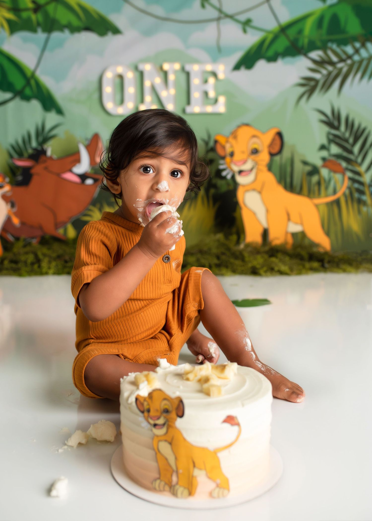 a boy sits in a lion king themed studio eating cake with his hands