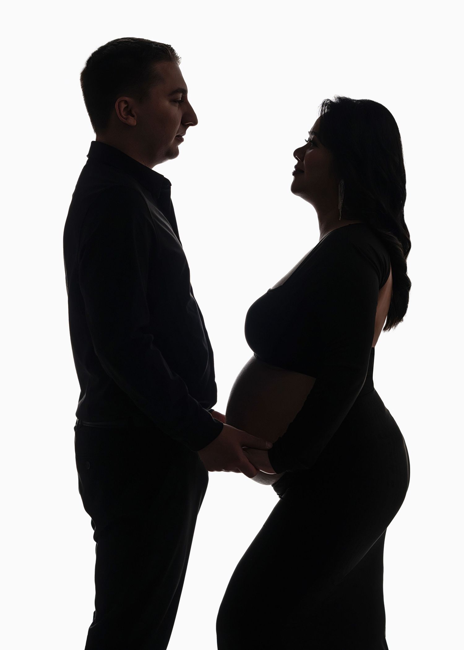 Silhouette profile view of couple in tender moment shows pregnant woman's belly against white background.