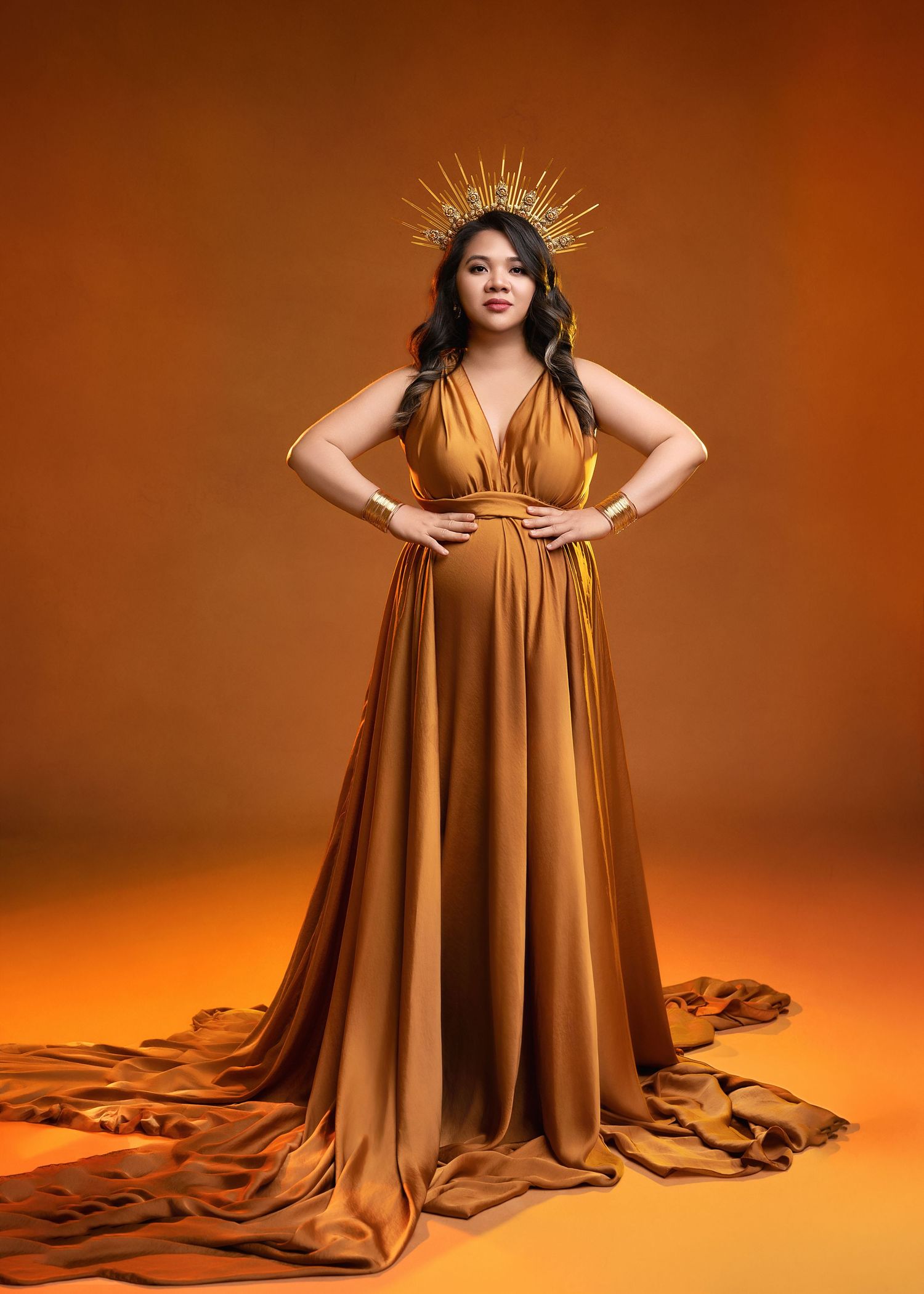 A woman in a luxurious flowing brown gown poses dramatically against an orange backdrop in a creative fashion series.