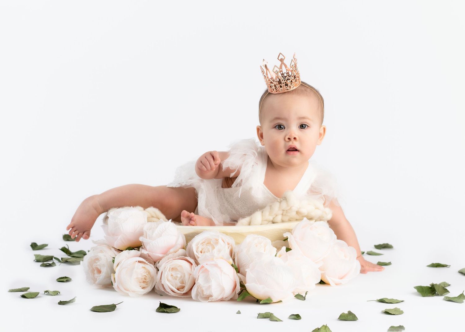 a baby sits in a basket surrounded by roses and greenery during a session with a minneapolis photographer