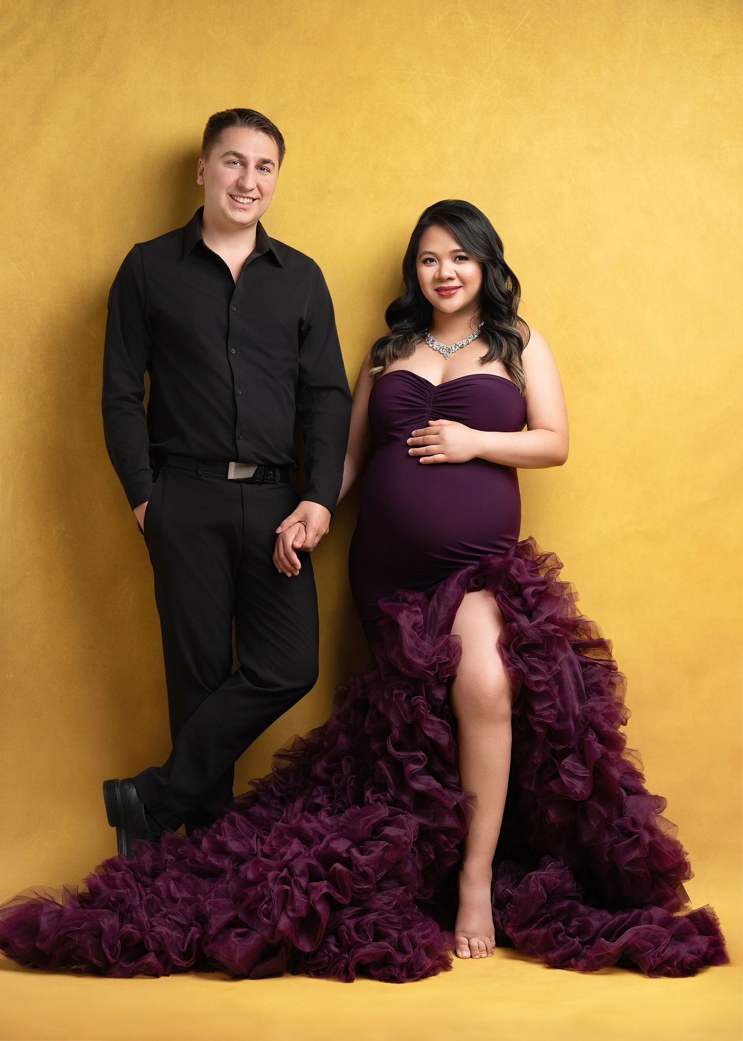 A couple in formal attire poses against a yellow backdrop for a series of romantic photos with a flowing purple dress.