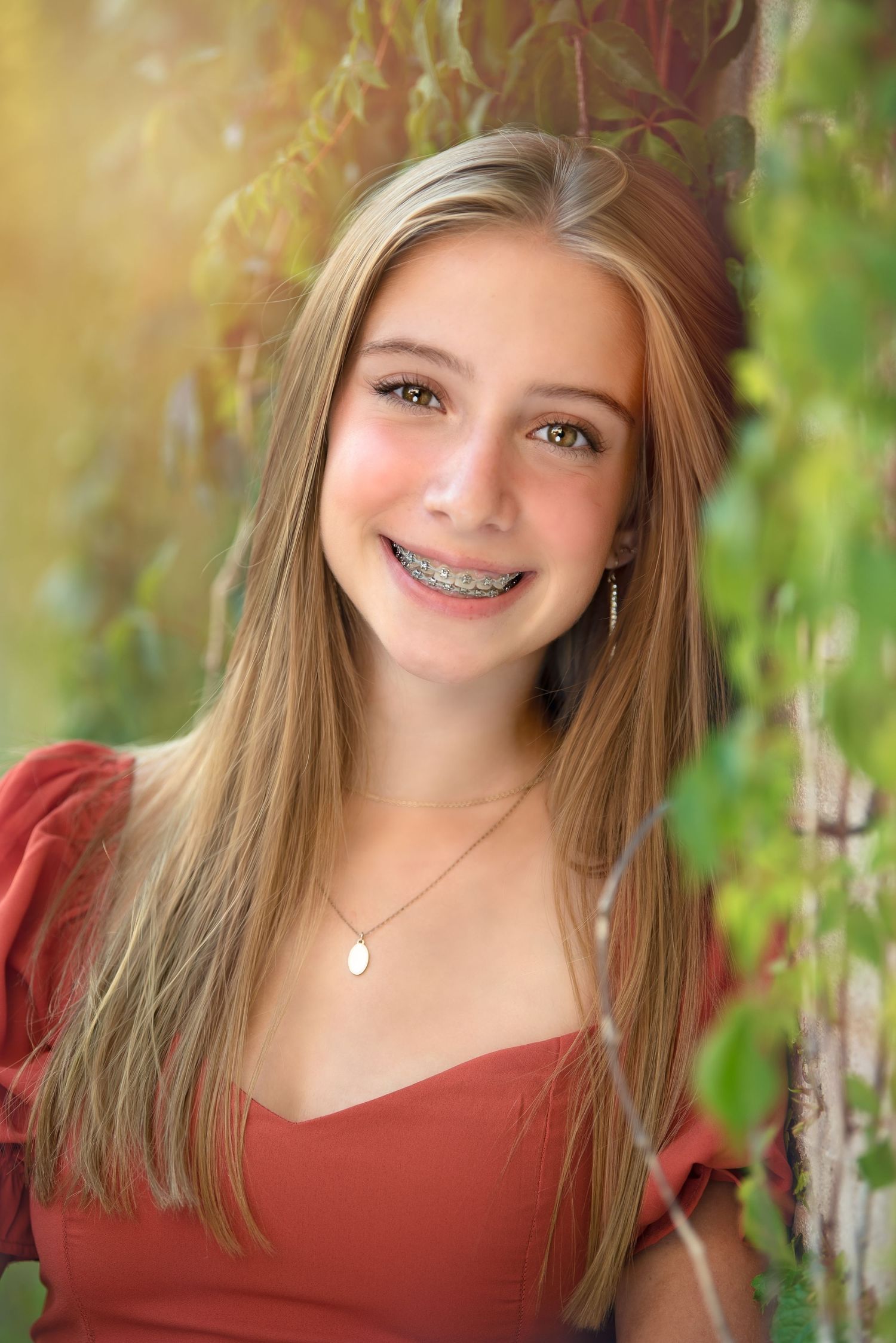 a young woman smiles while leaning against a wall covered in greenery