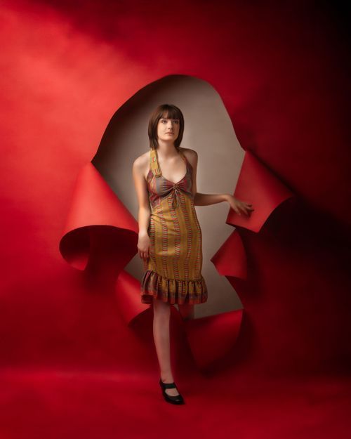 minneapolis senior photography of a girl in a brown ruffled dress posed in front of a torn red paper backdrop in a studio setting