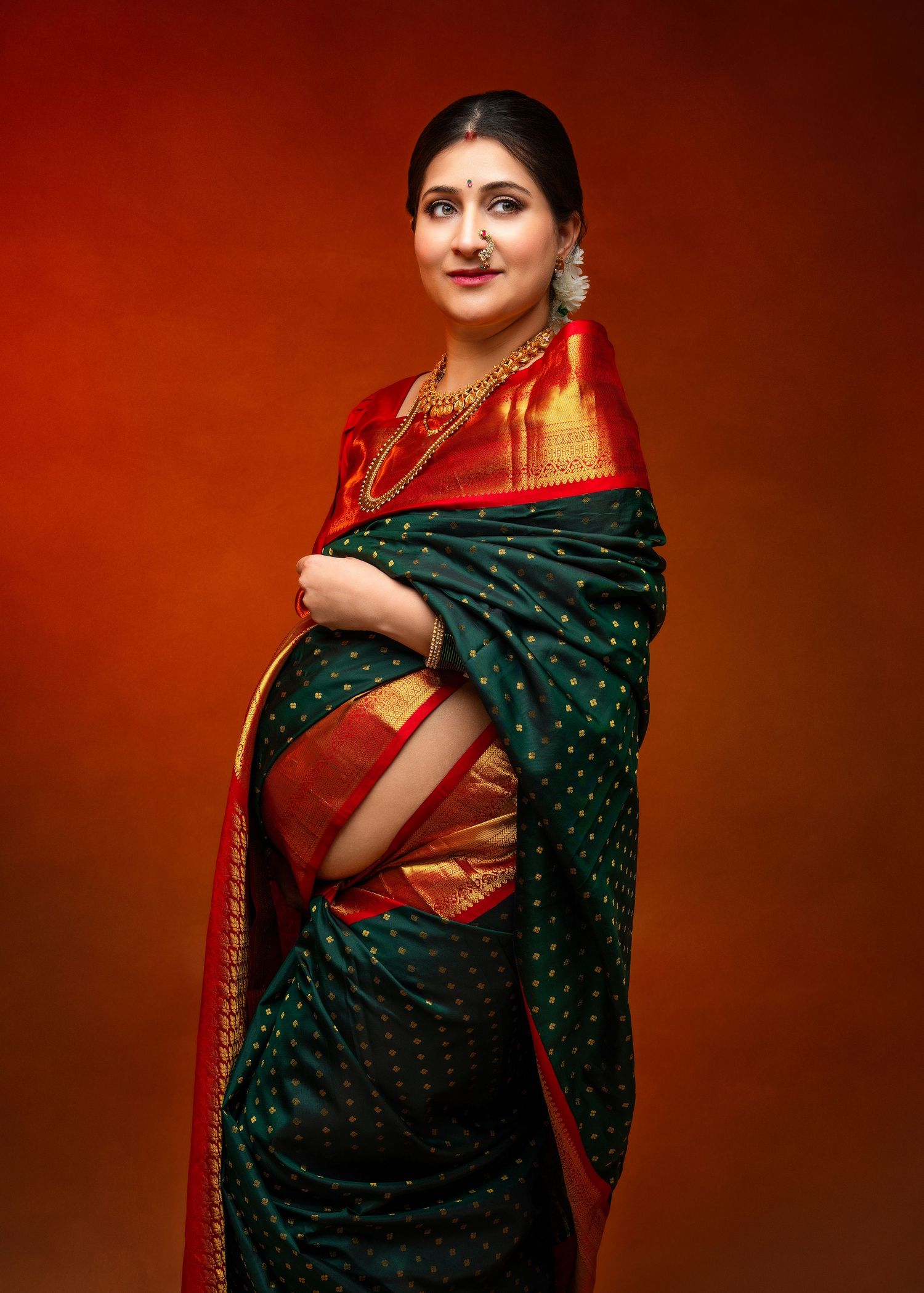 A portrait showing a woman in traditional Indian attire, wearing a dark green saree with red and gold accents