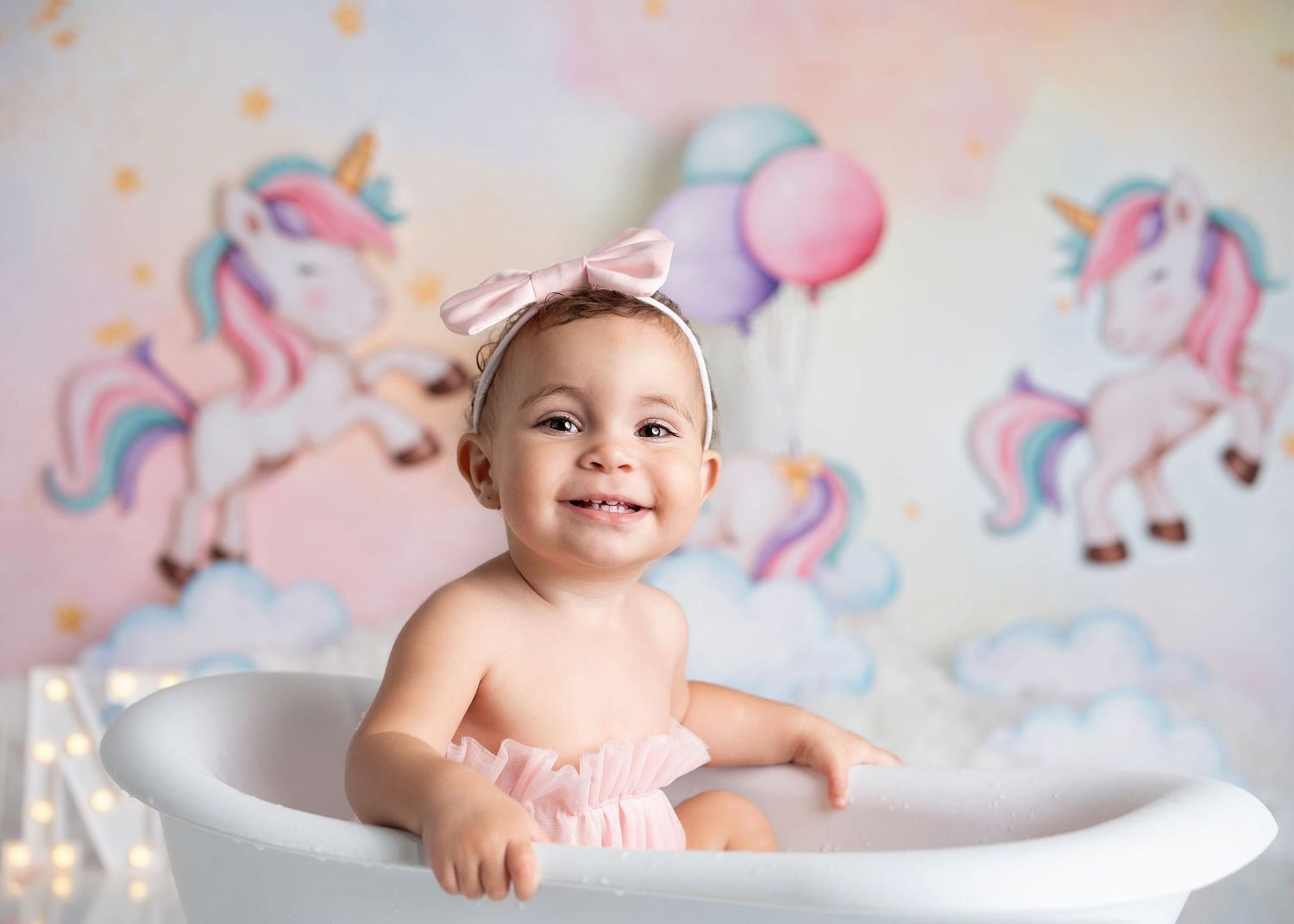 Unicorn themed baby photoshoot setup with pink and pastel decorations in bathtub setting.