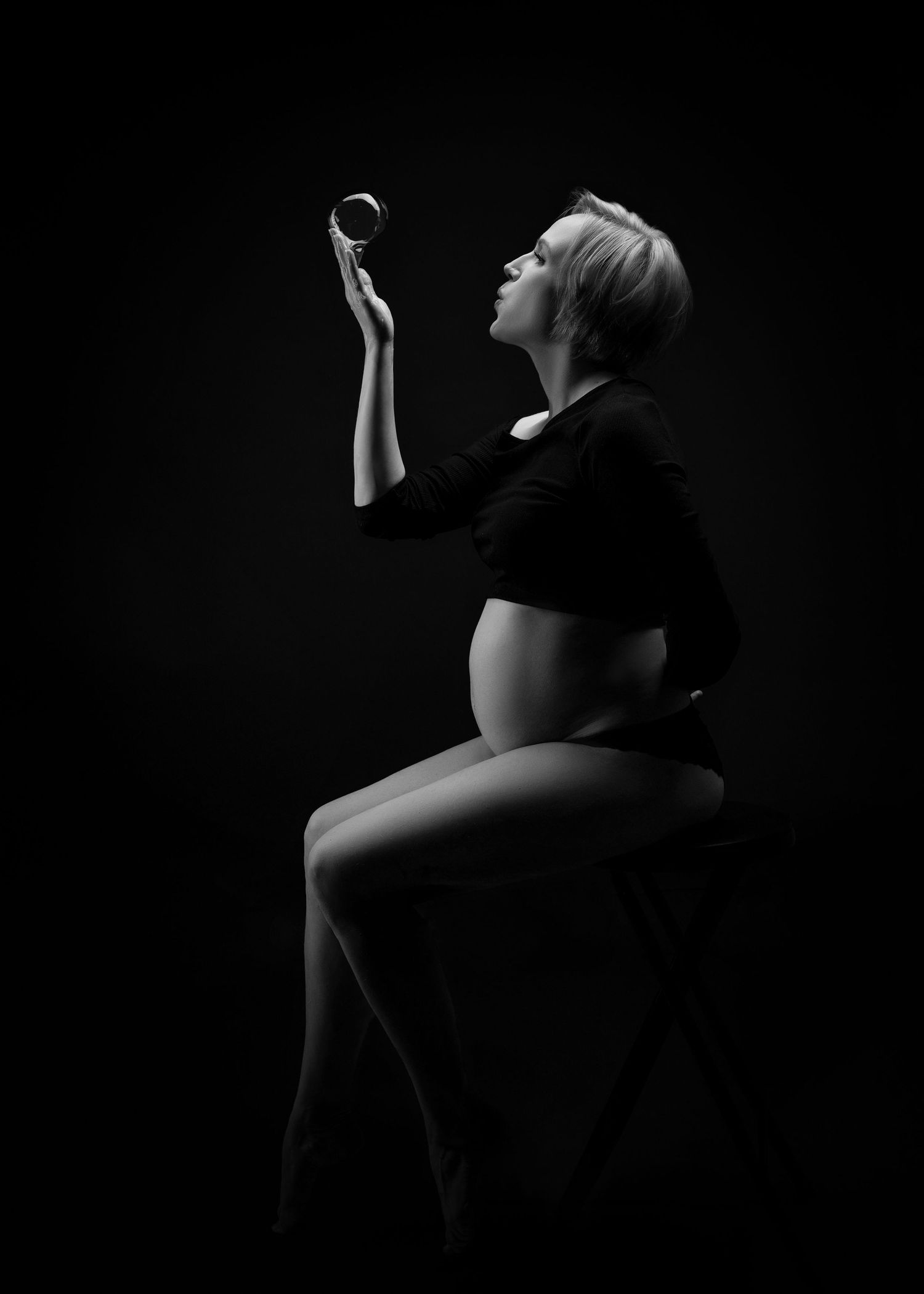 a pregnant woman sits in dramatic dark lighting with a bubble balanced on her fingertips