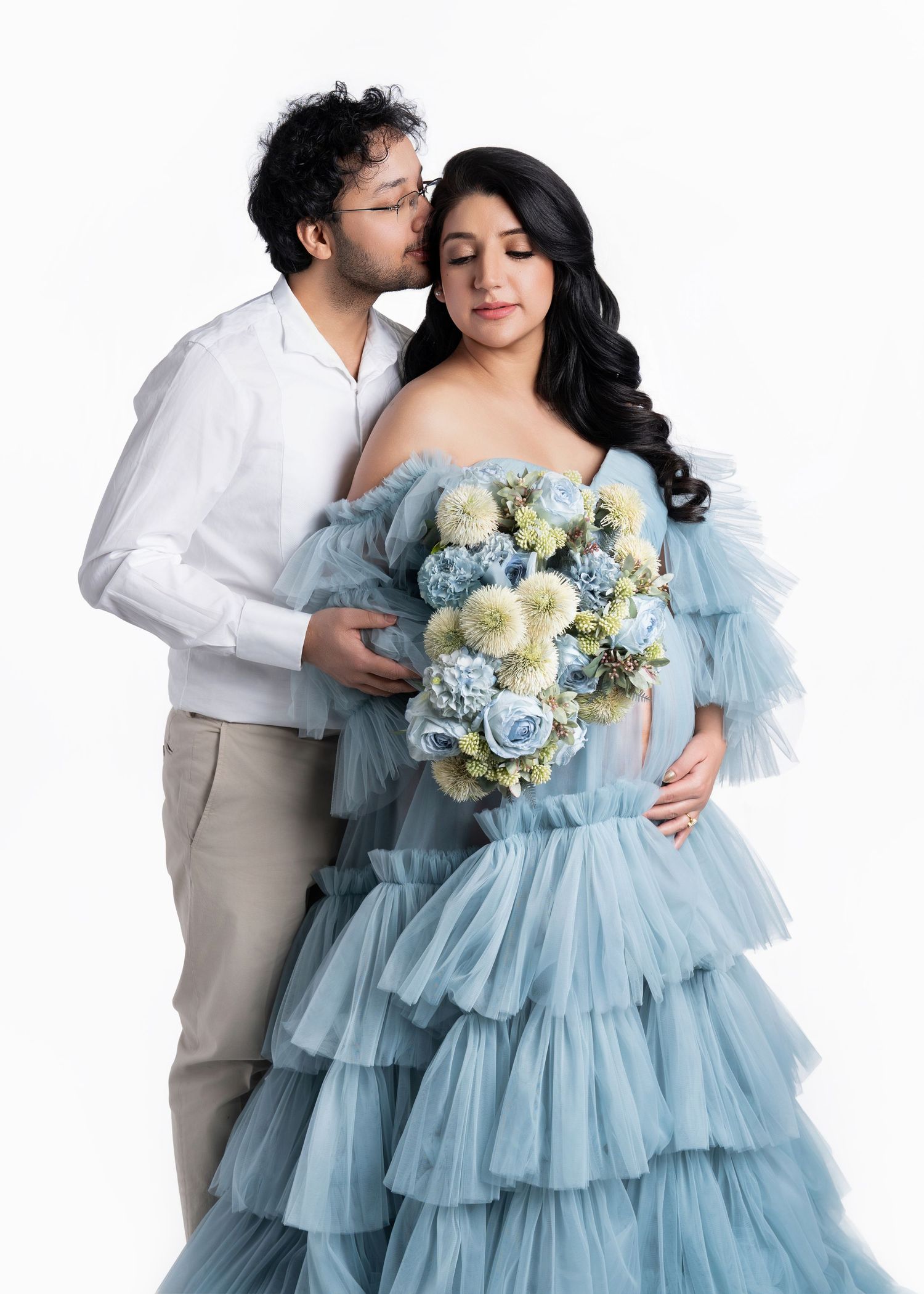 Couple poses together with woman in light blue tulle dress holding white flowers.