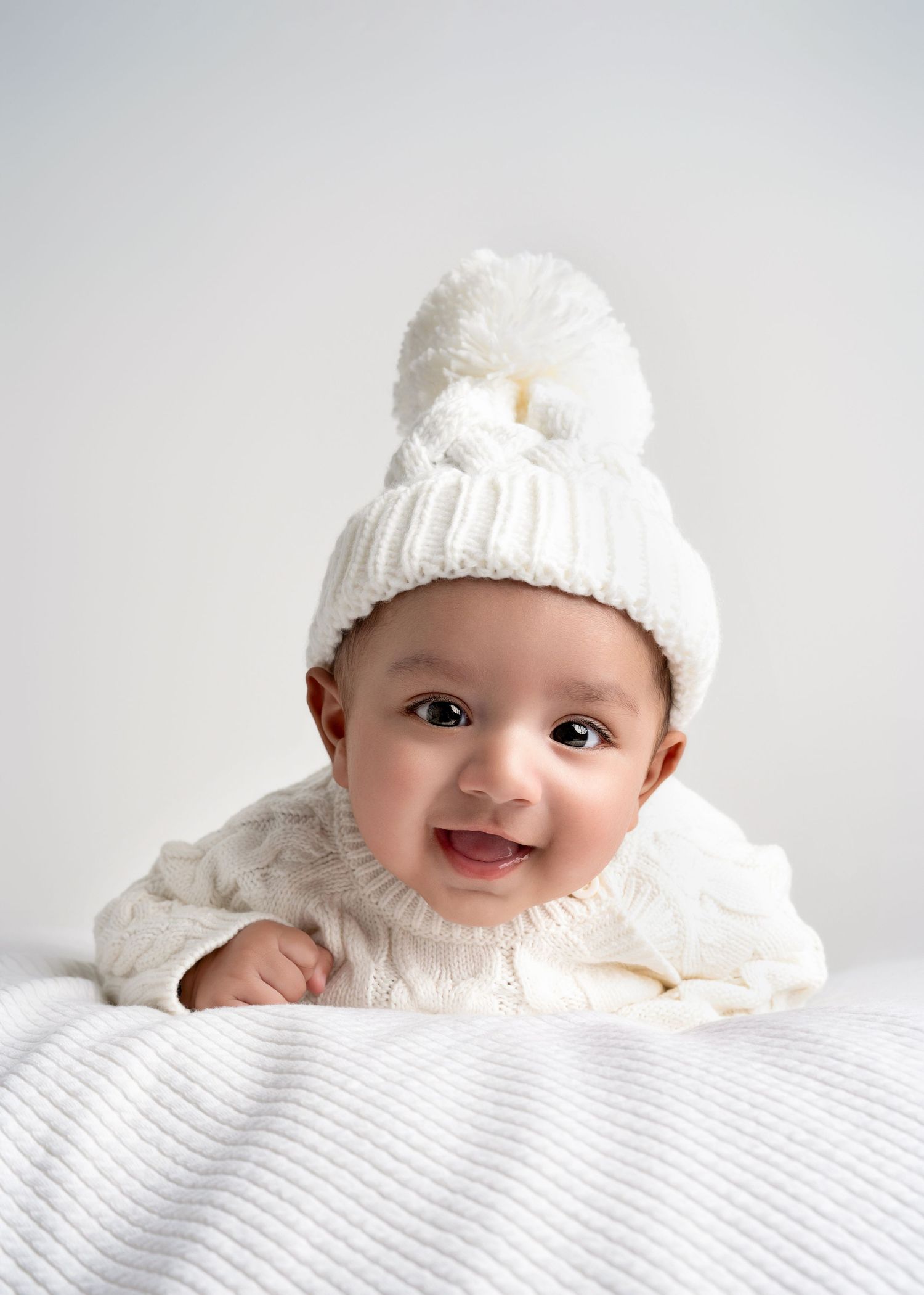 a baby lays on a blanket wearing all white