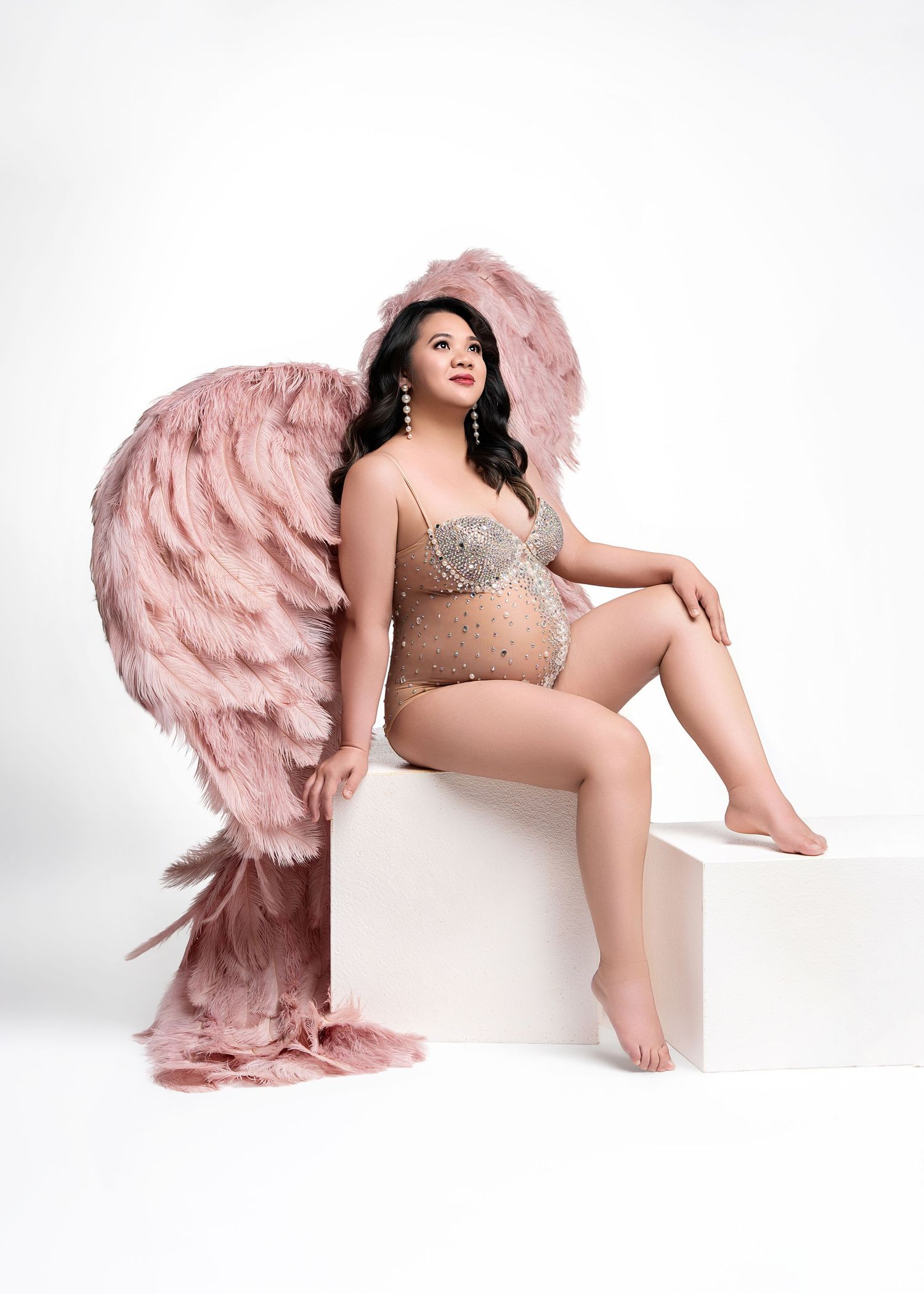 A graceful figure poses in a tulle pink gown with feathered details against a white backdrop.