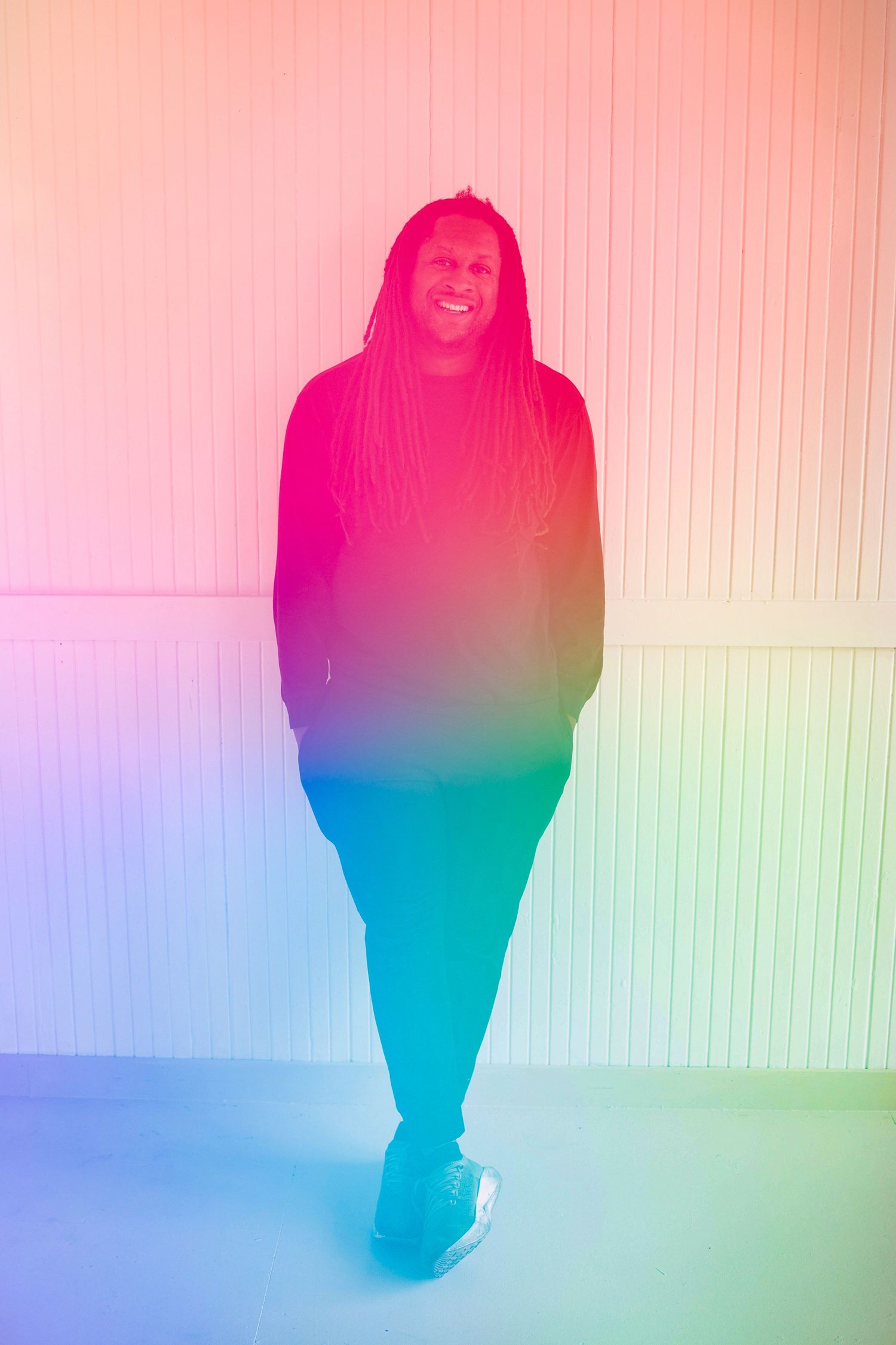 A person stands in a color gradient background transitioning from orange and pink to blue and green tones.