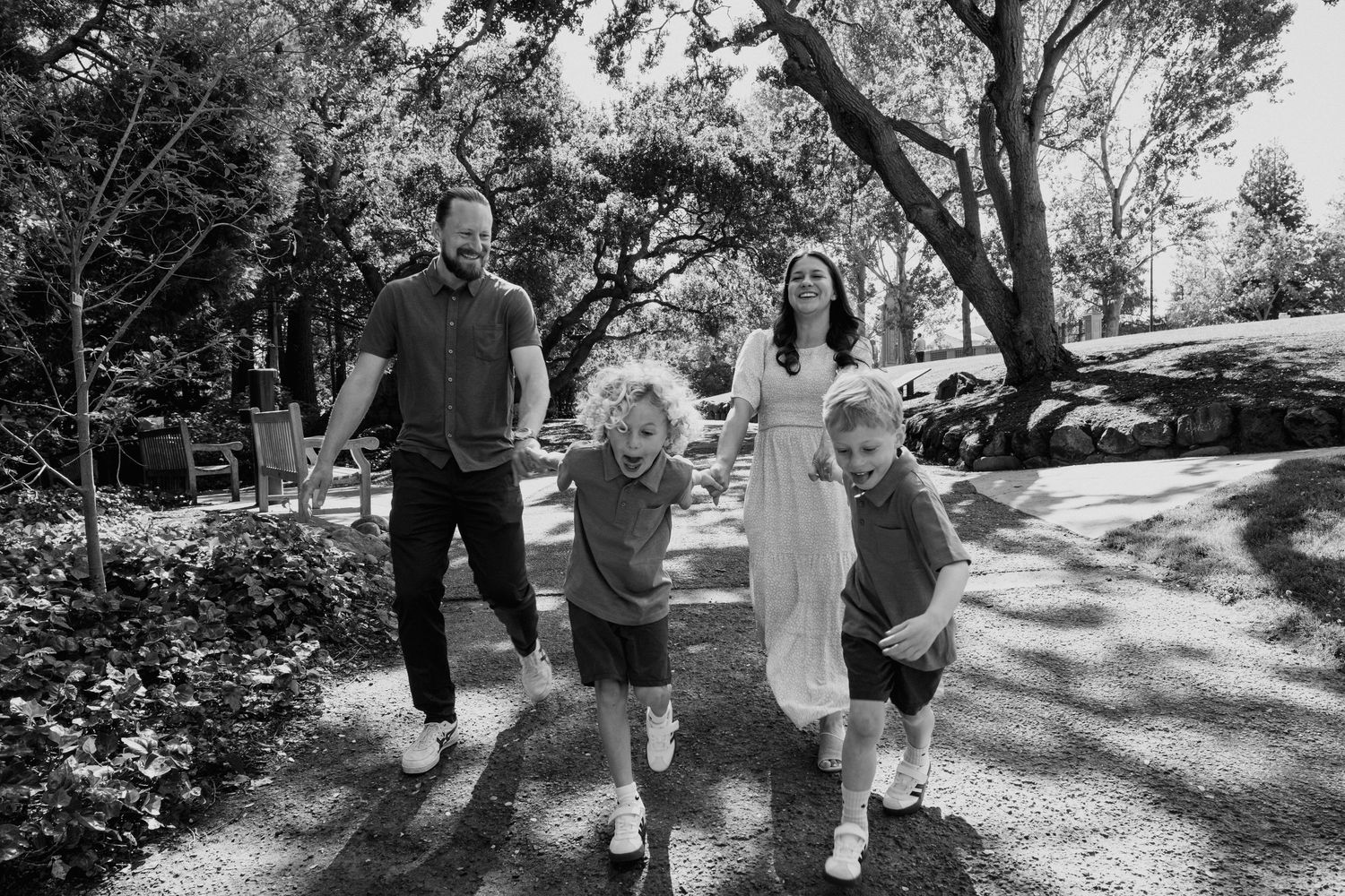 Family of four walking together on a sundrenched garden path during a casual outdoor photo session.