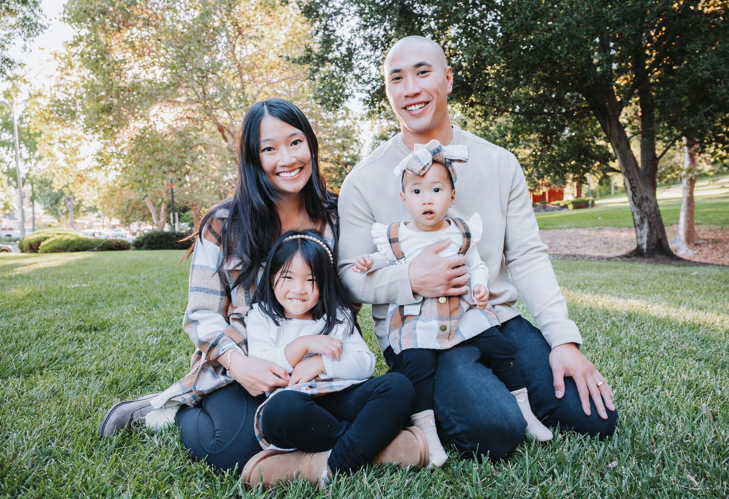 A family sits together on green grass during a warm autumn day in the park.