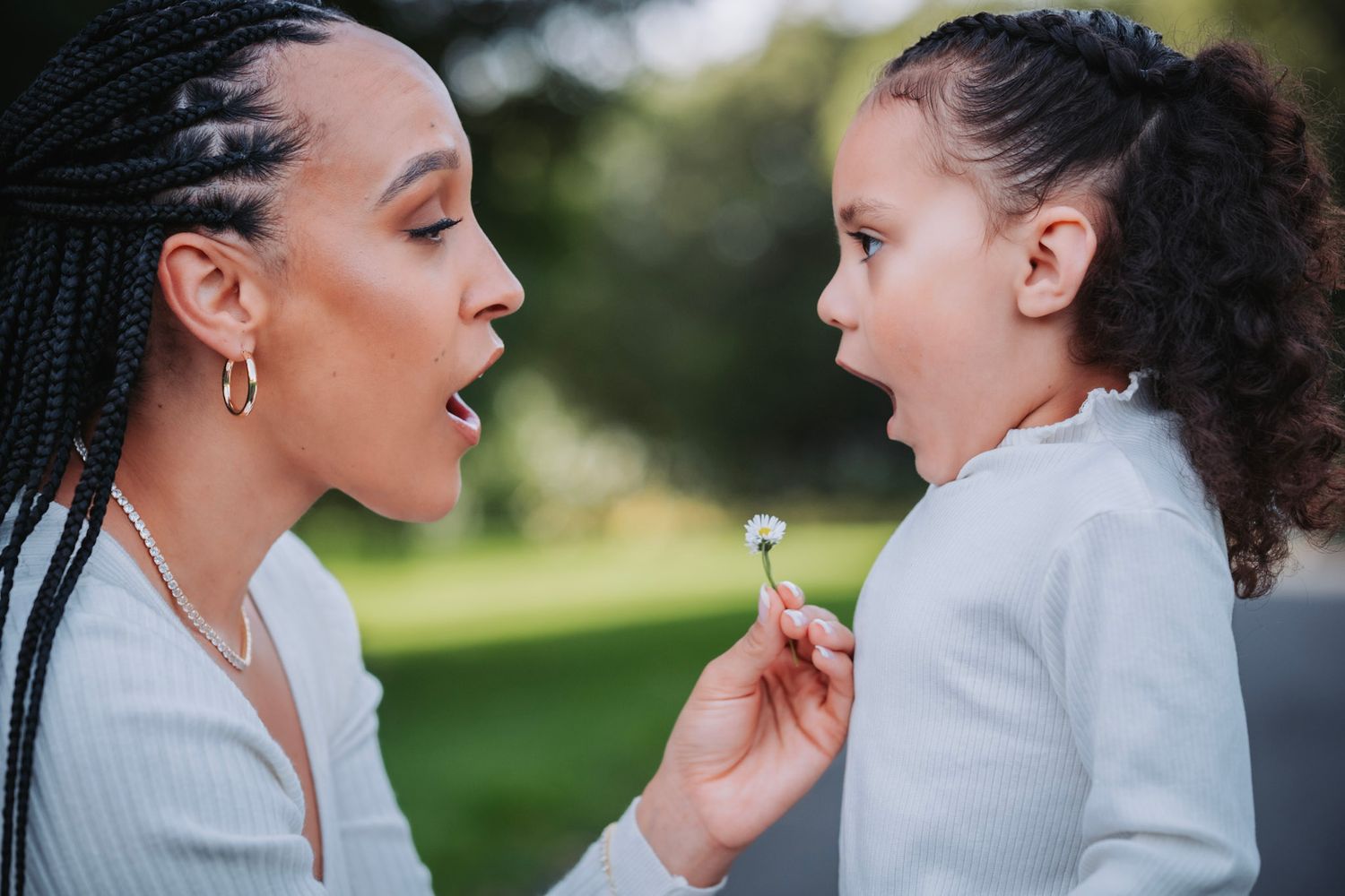 Two people share a sweet moment outdoors as they interact closely with a dandelion flower in a sunlit park.