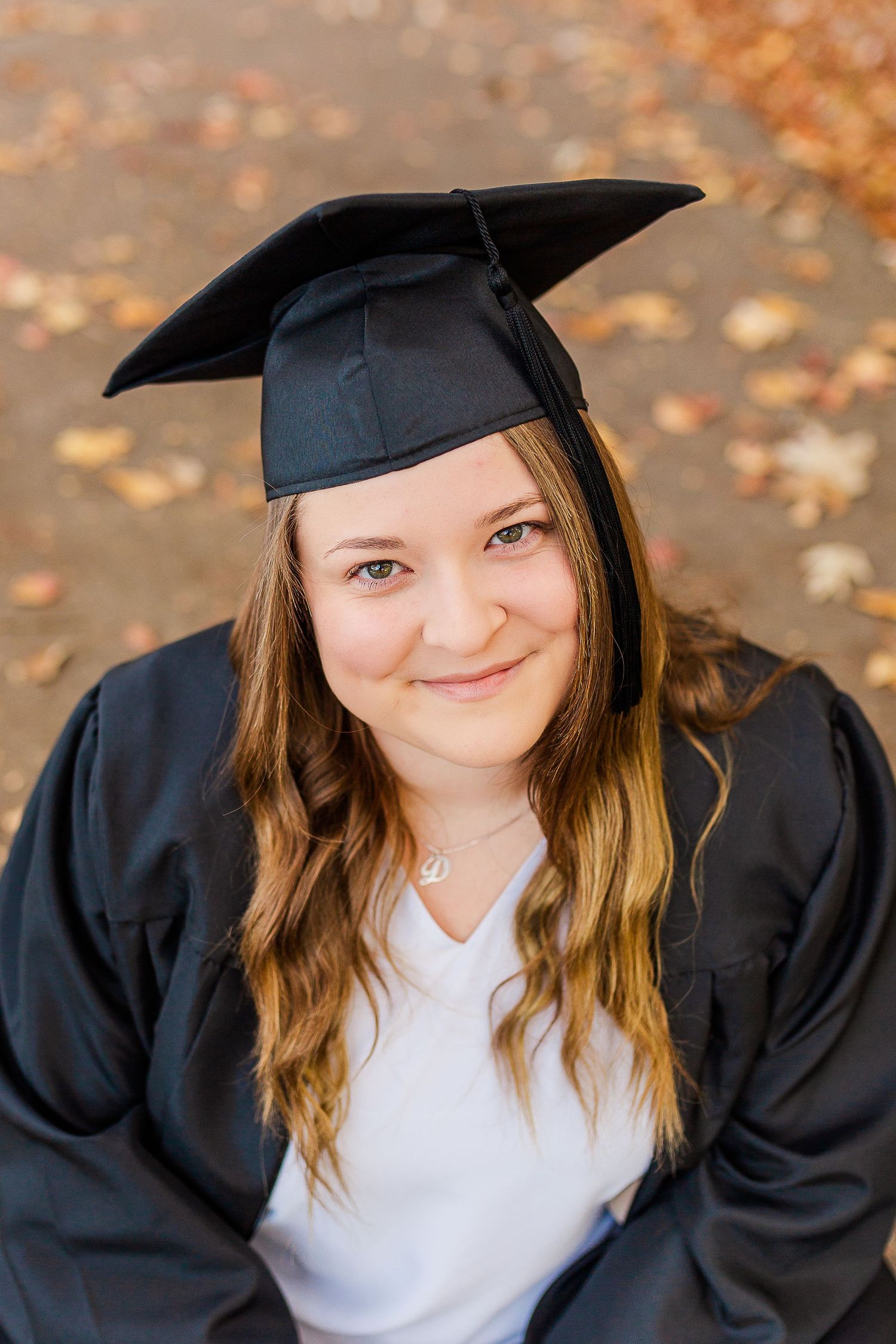Graduate in cap and gown poses for portrait during autumn season.
