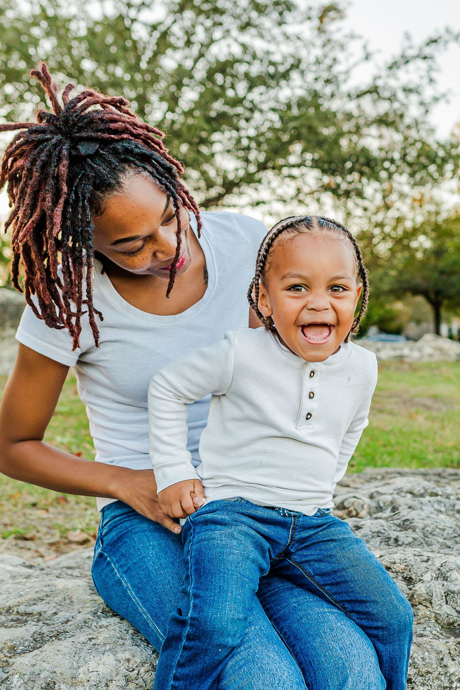 A parent and child share a joyful moment together outdoors while sitting on rocks in a natural setting.