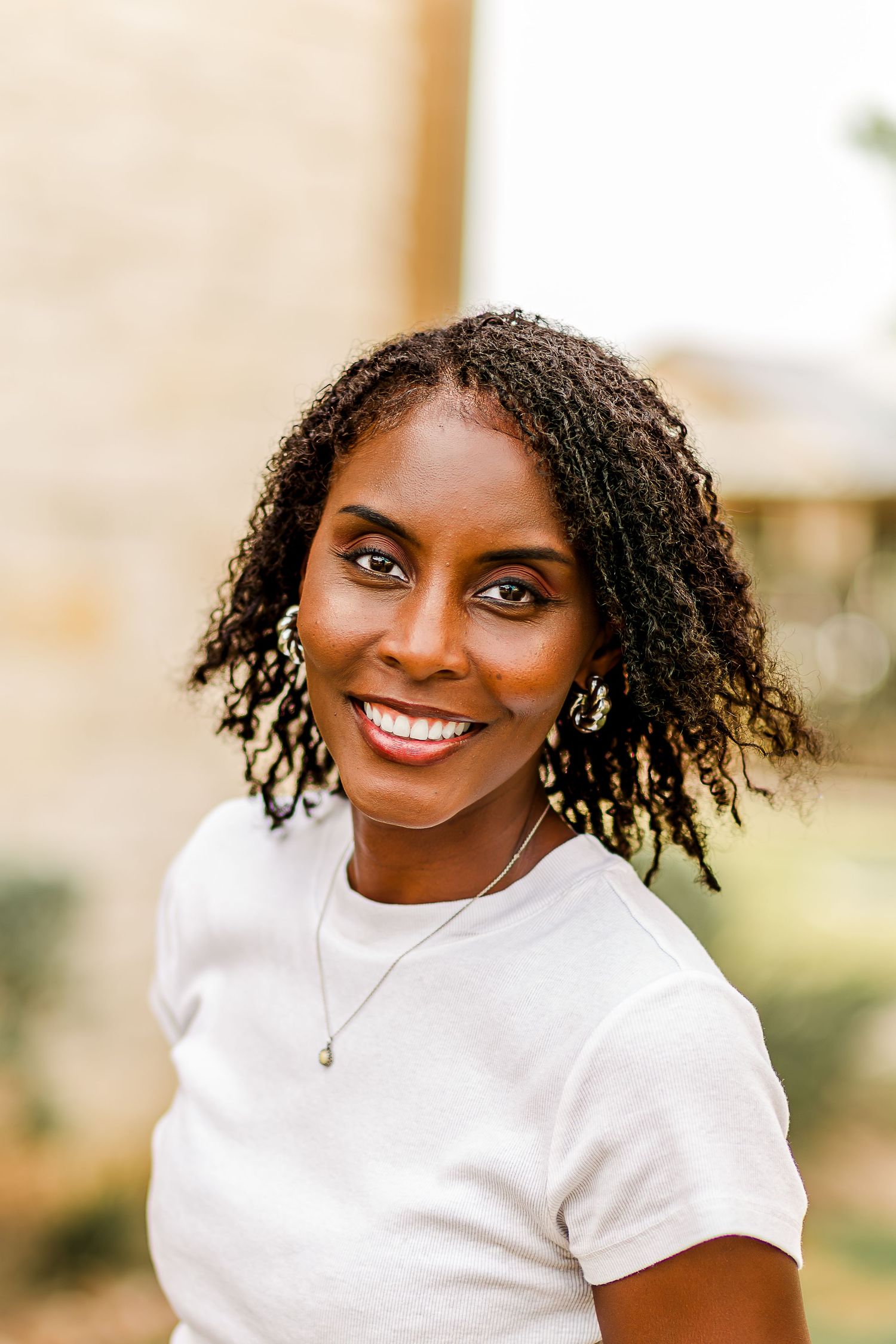 A series of four headshots showing someone with curly hair wearing a white t-shirt and smiling warmly at the camera.