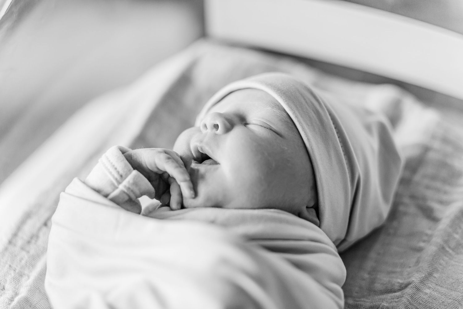 Black and white portrait of a newborn baby swaddled in white blankets sleeping peacefully.