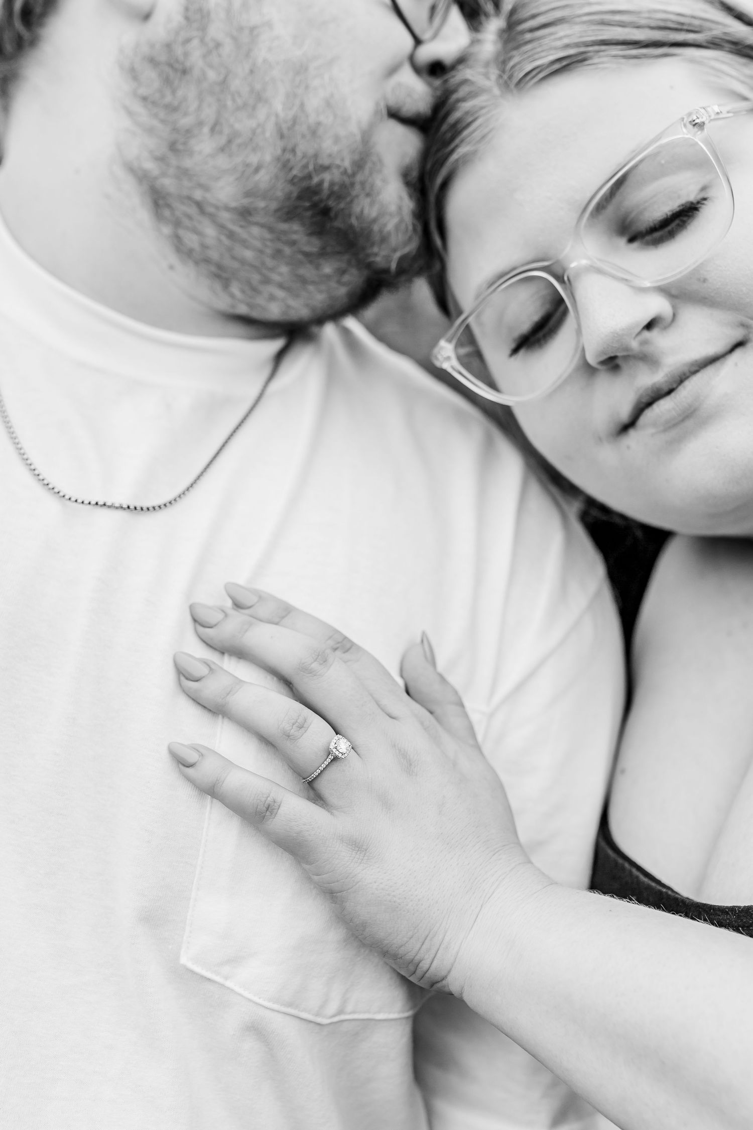 Intimate black and white photograph showing a tender romantic embrace with hands softly touching and rings visible.