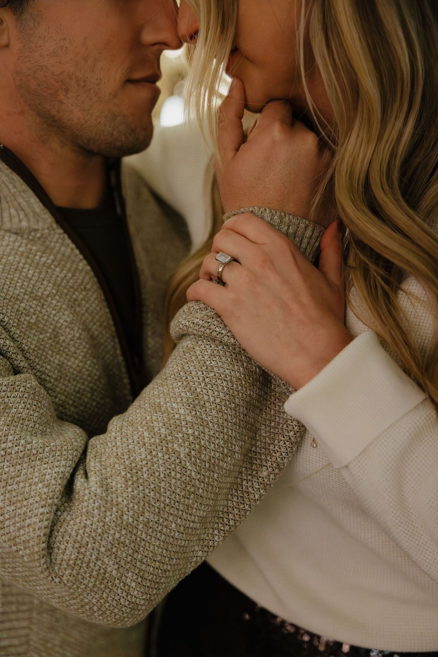 Close-up of a couple sharing a romantic moment, woman displaying a diamond engagement ring on her hand.