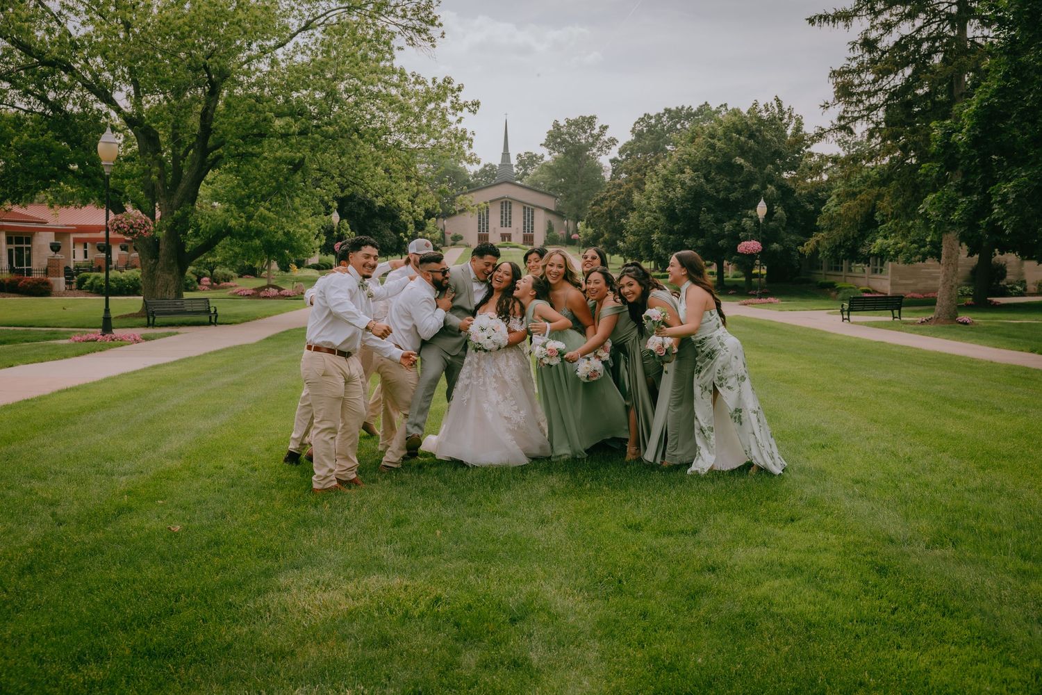 A wedding party joyfully runs across a lush green lawn on a sunny summer day.