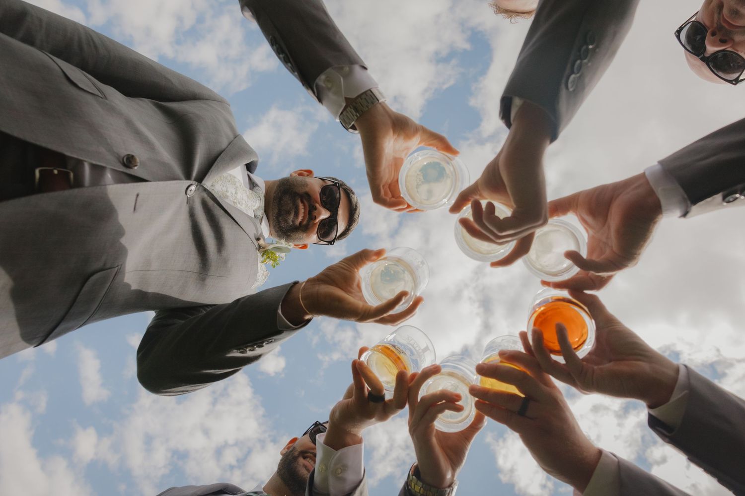 Low angle shot of wedding party members raising champagne glasses against blue sky.