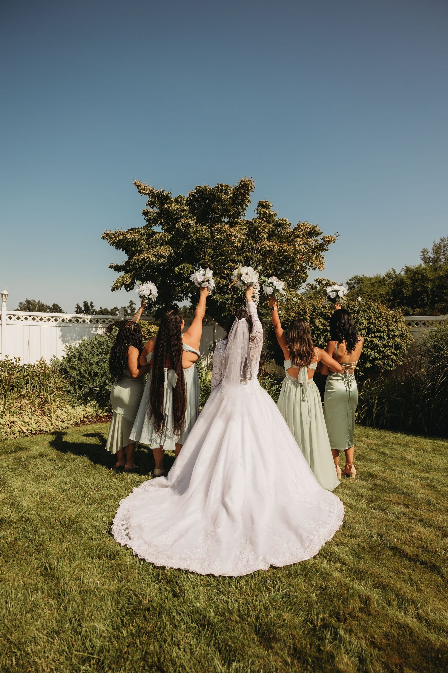 Bridesmaids in sage green dresses celebrate outdoors with wedding party.