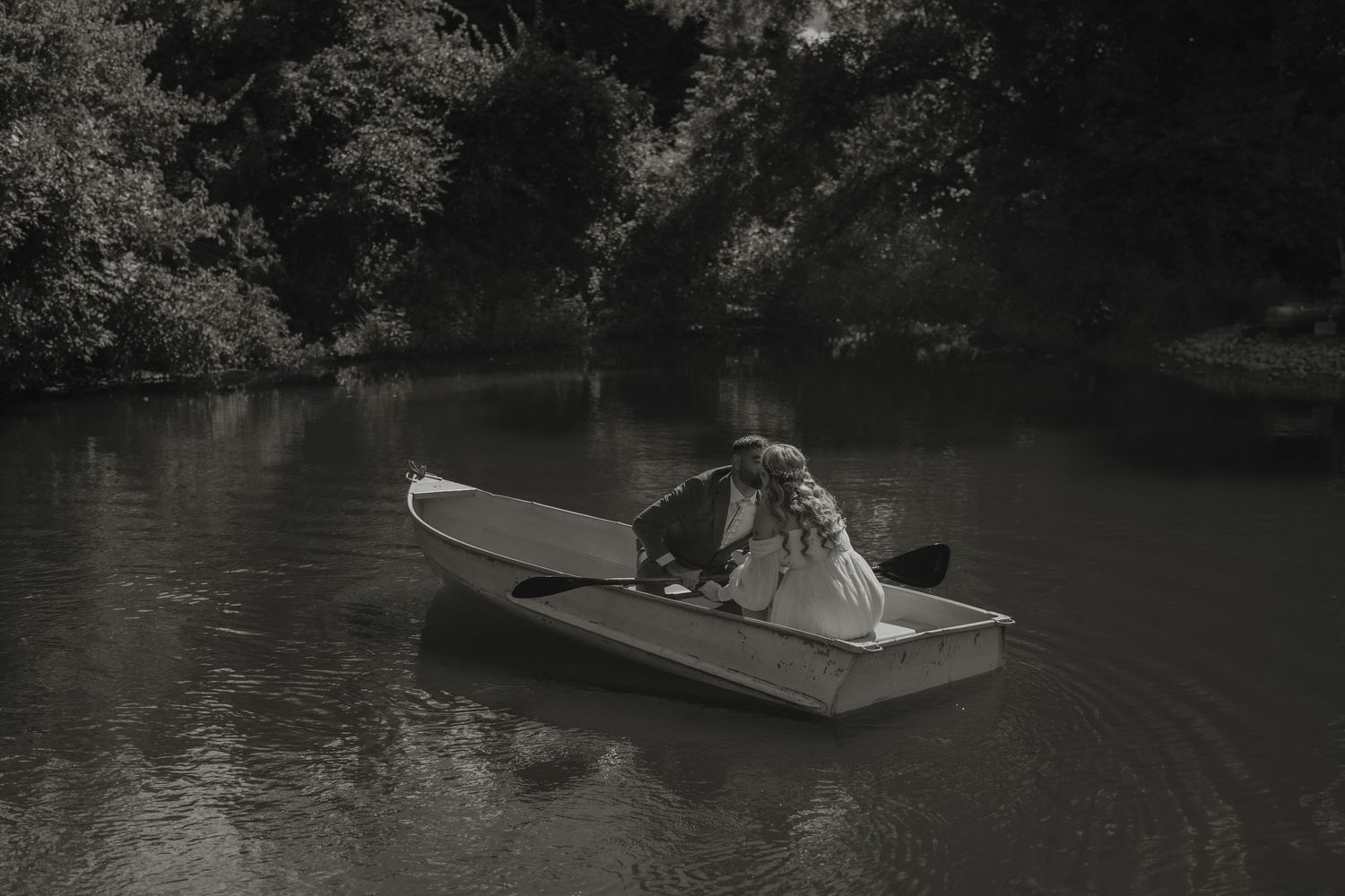 Small wooden boat drifts peacefully across dark waters surrounded by lush green trees and foliage.