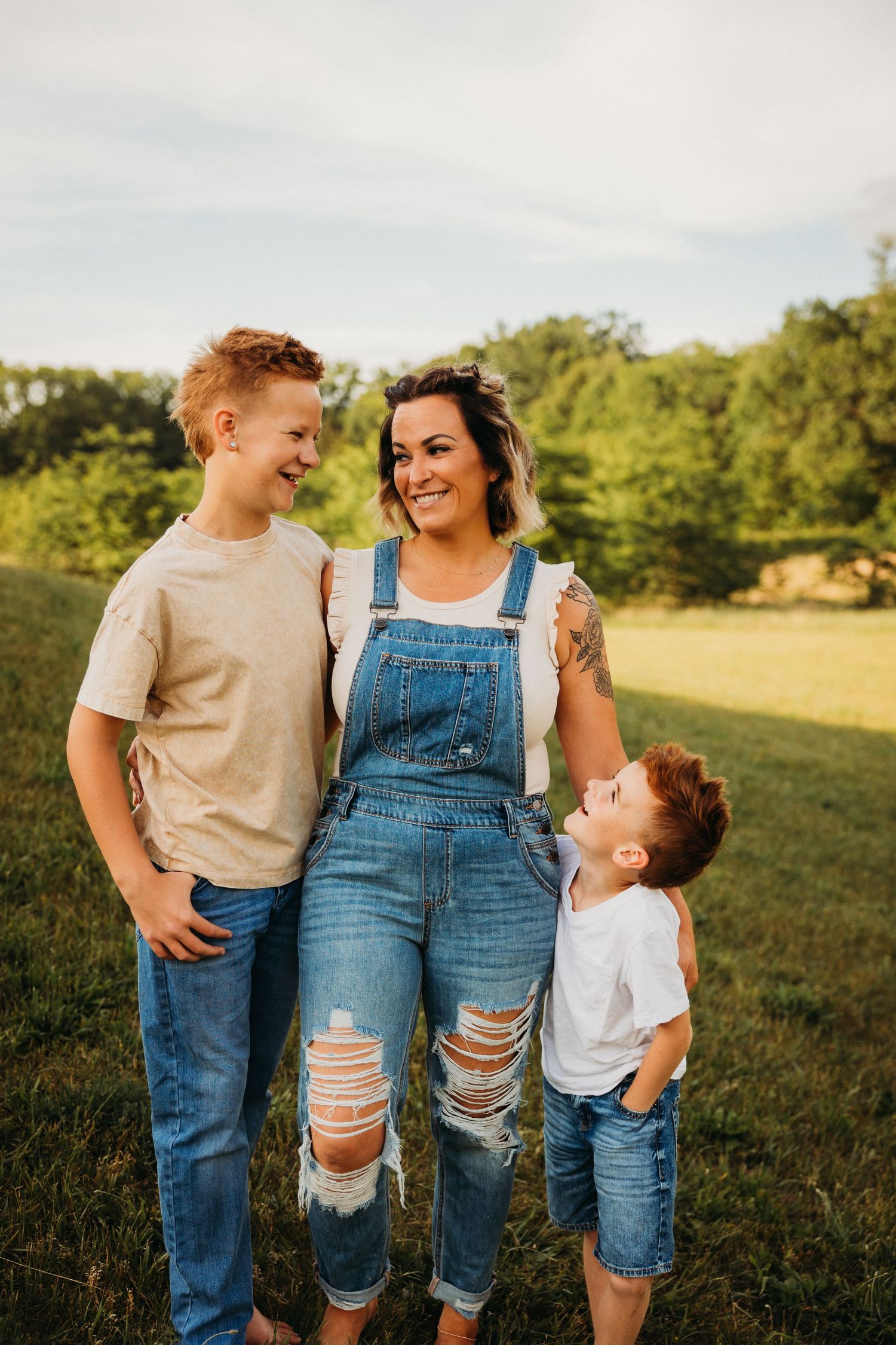 Group in casual denim and t-shirts poses together on grassy field during golden hour.